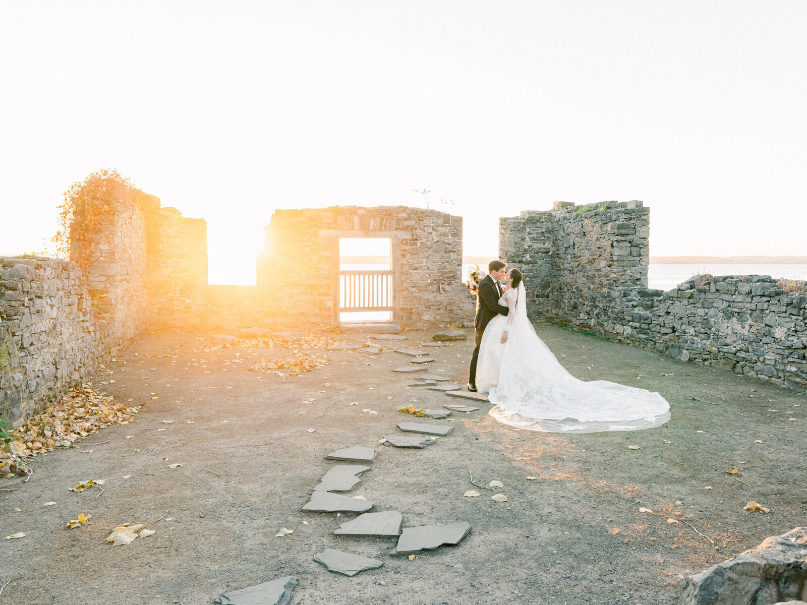 A wedding couple shares a kiss in stone ruins as the sun glows through.