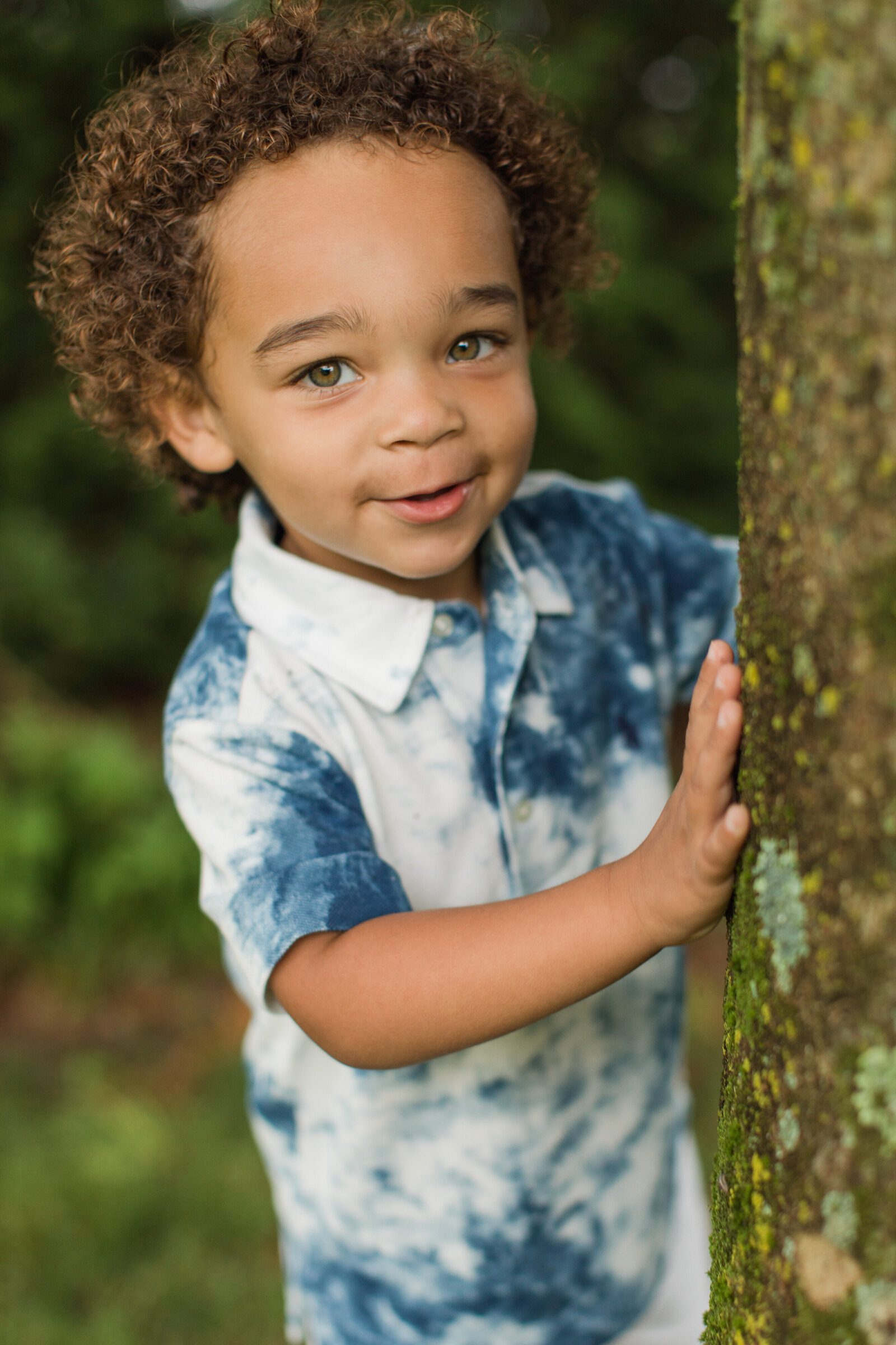 little boy peeking around a tree