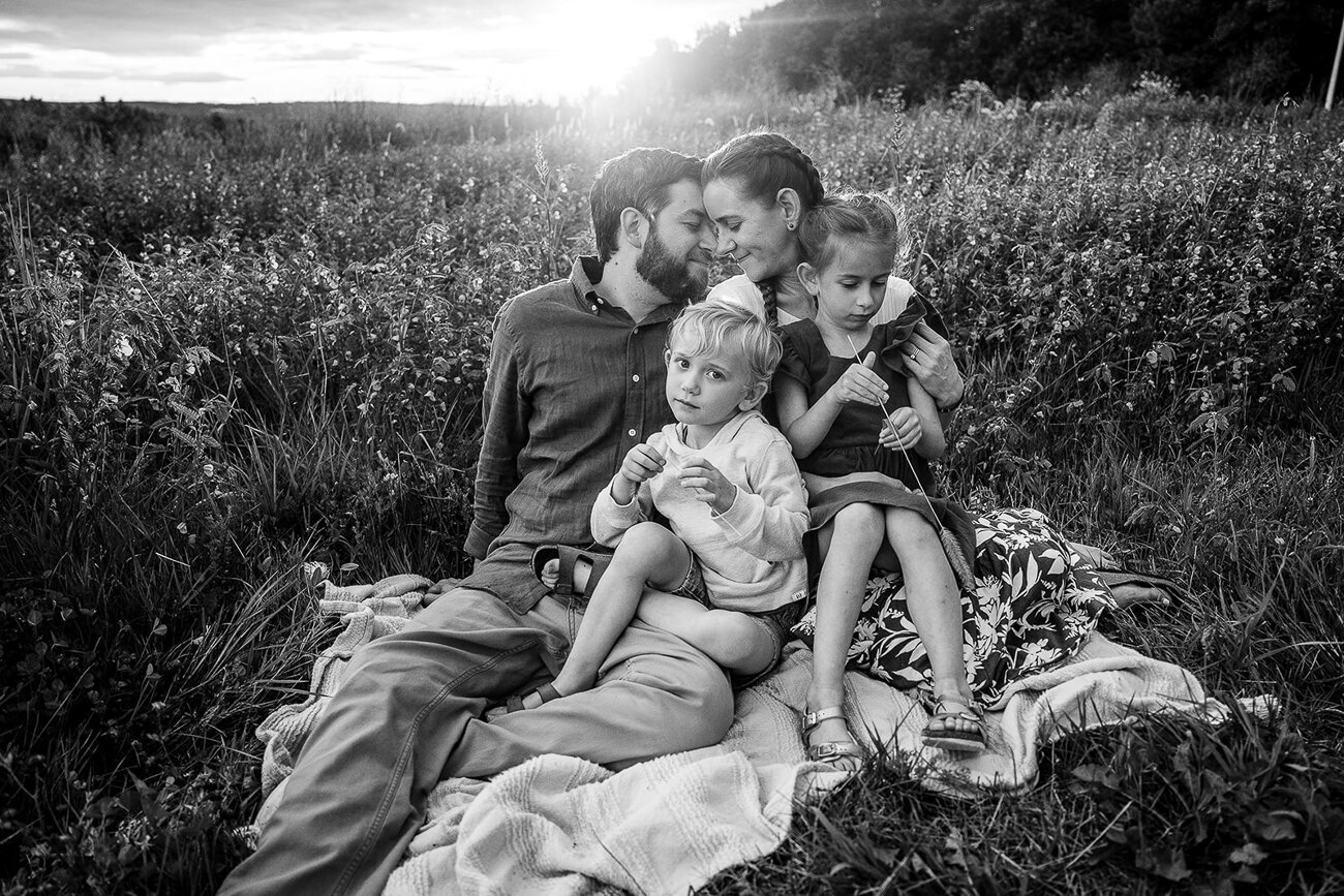 black and white image of family of four snuggling on blanket in sunset field