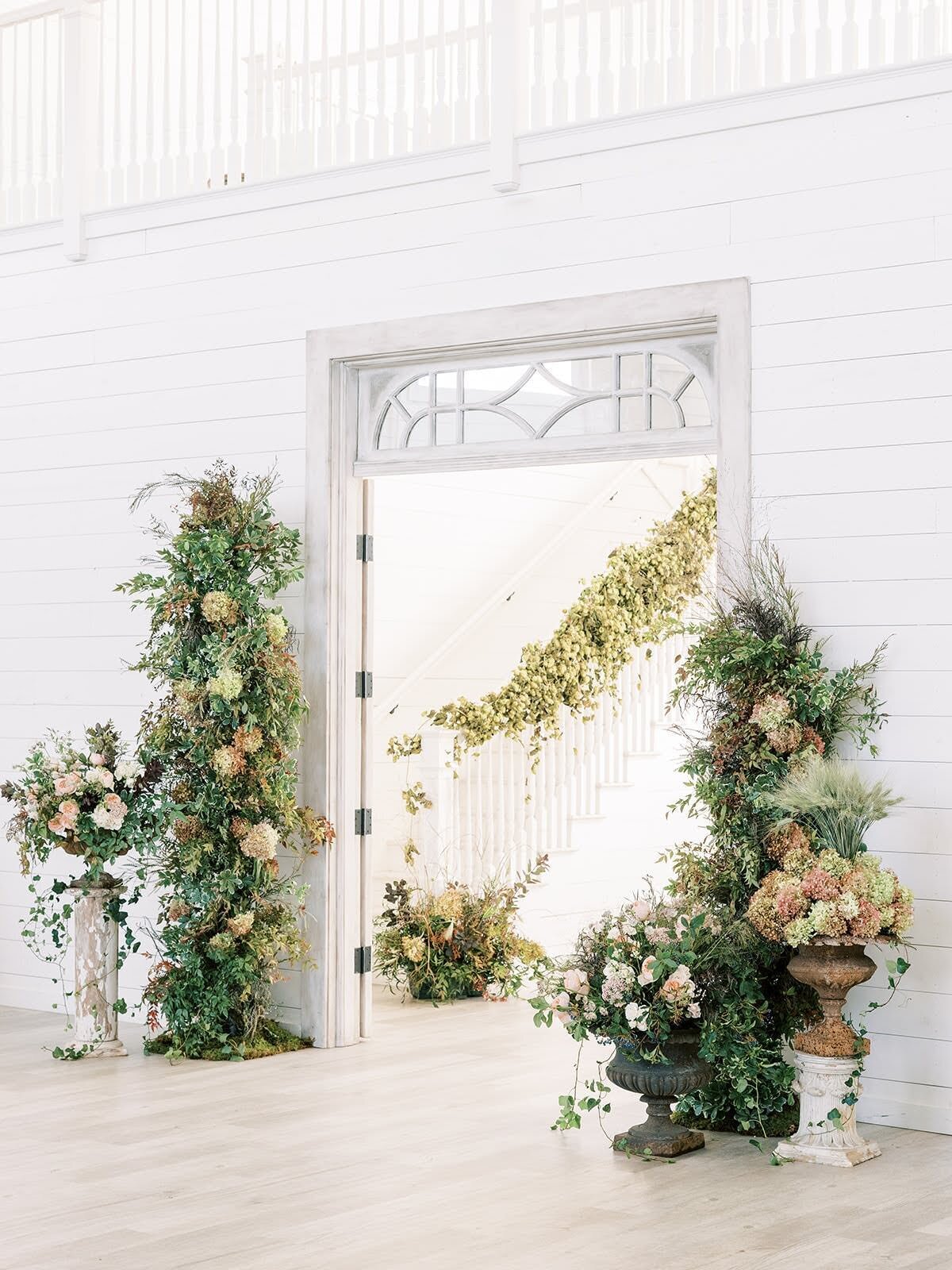 White french doors open to showcase a staircase decorated with lush floral installation