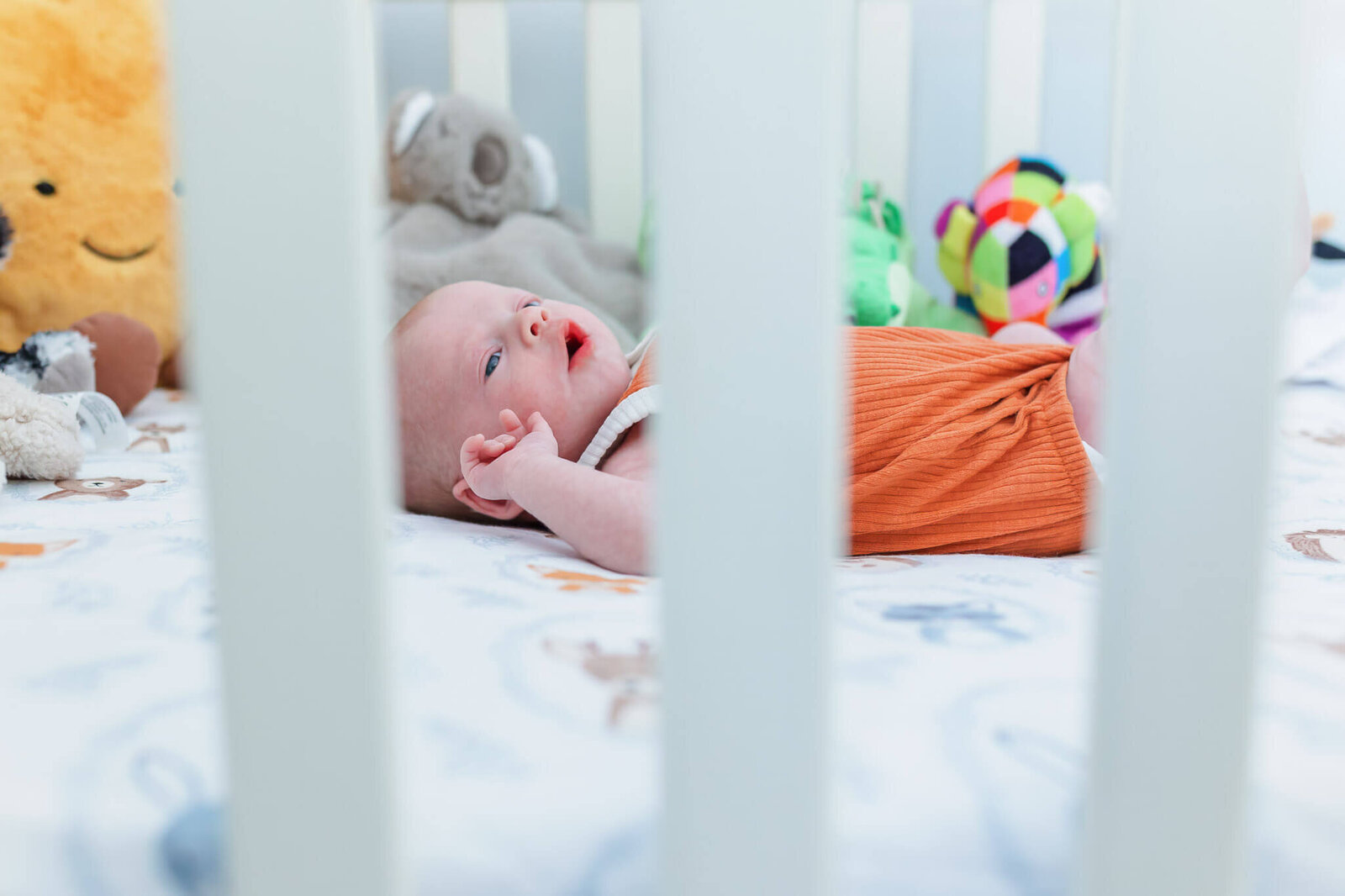 A peak through the crib bars at the newborn baby in the crib.
