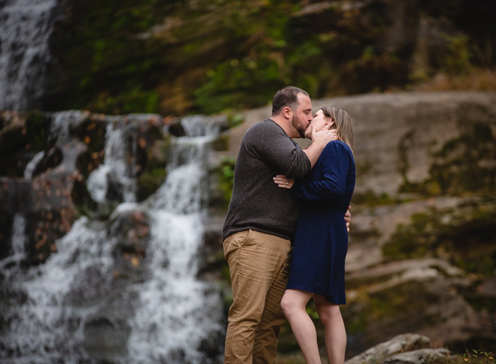 engaged couple kissing in front of a waterfall