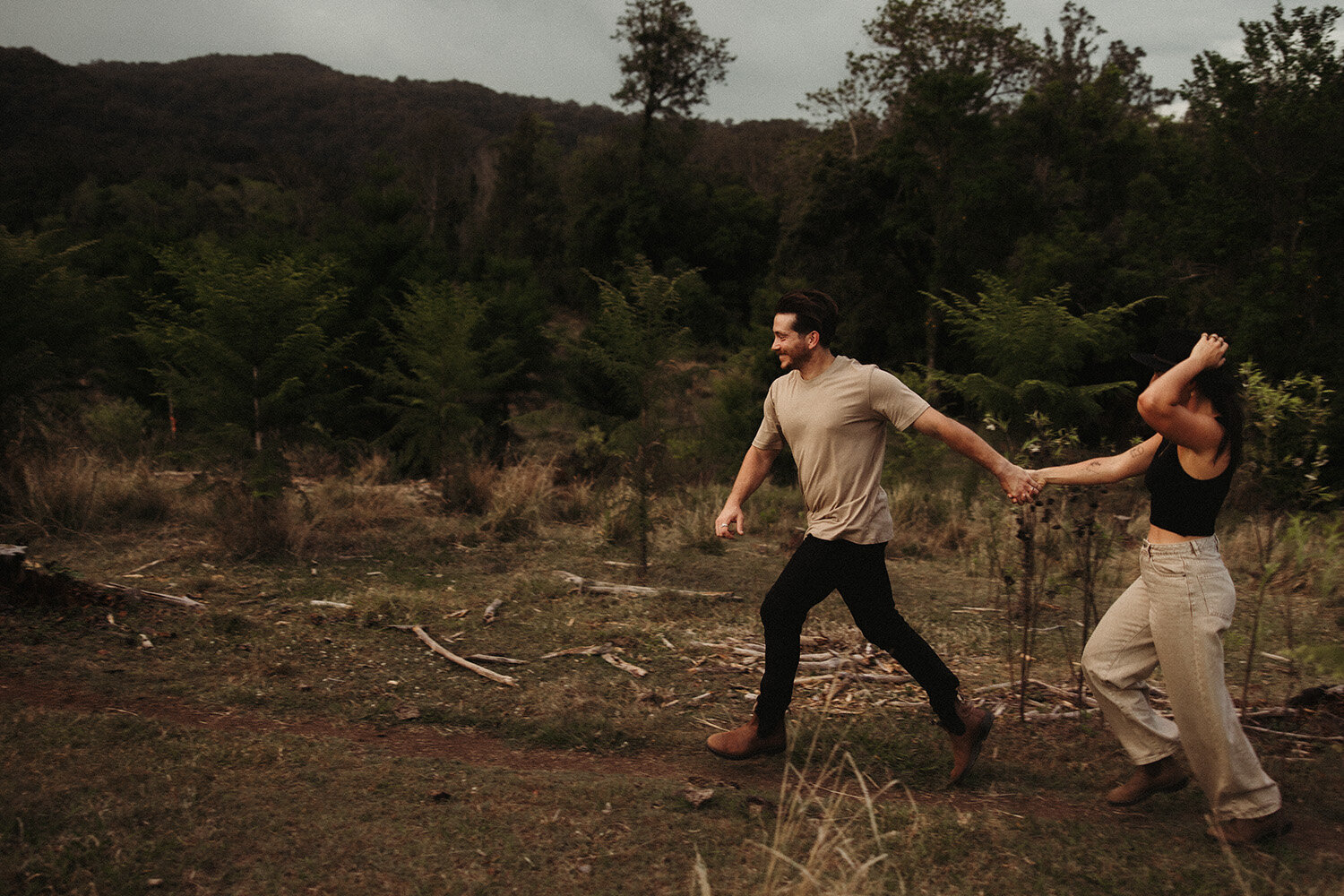 Playful couple holding hands and running through a field captured by Sunshine Coast photographer