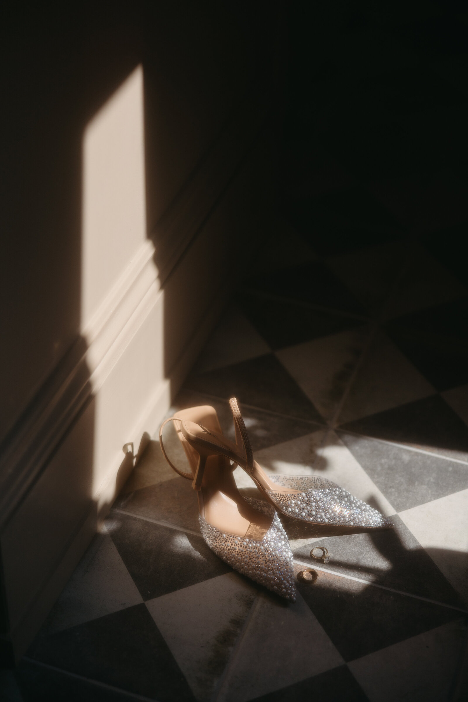 A beautiful detail photo of a pair of bridal shoes and wedding rings laid out on a tile floor at a wedding in Newfoundland. 