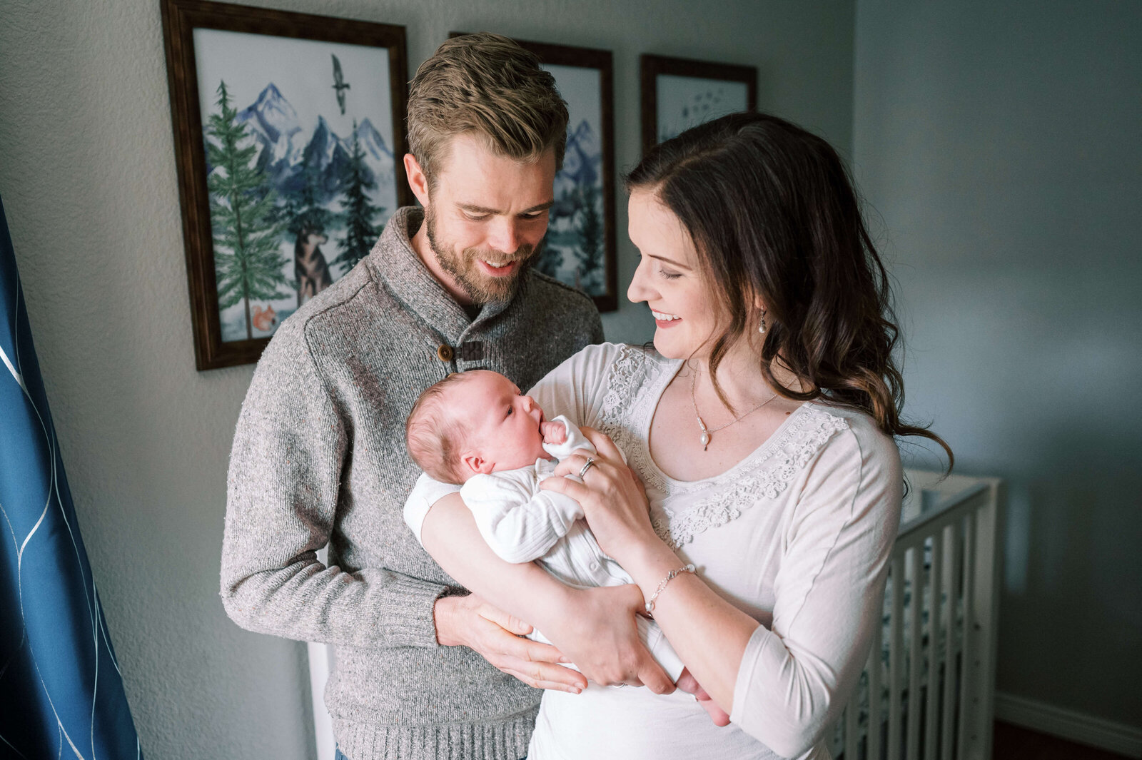 While standing in their woodland themed nursery, a new family admires their baby son