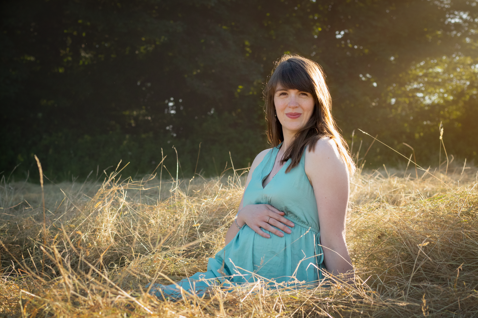 Mum to be in blue dress sits for maternity photography in field of hay