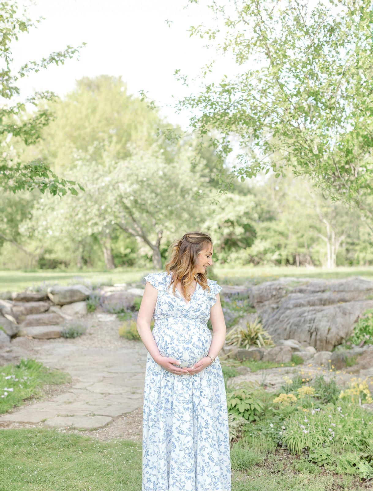 pregnant woman wearing blue floral dress cradles baby bump and smiles while looking over her shoulder