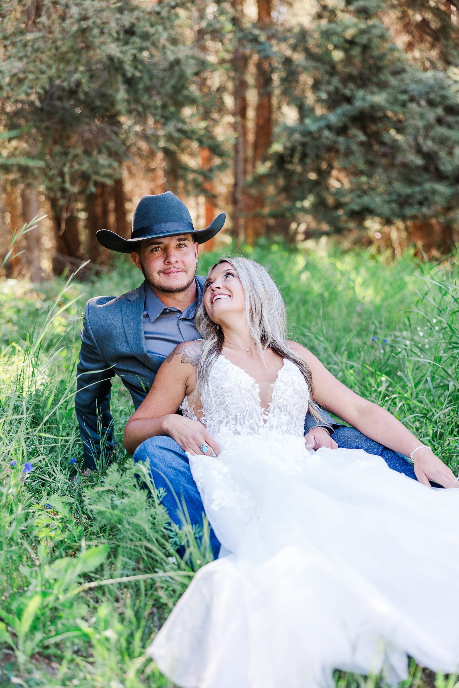 Bride and groom sit together in a grassy field at their wedding at Arrowhead Lodge