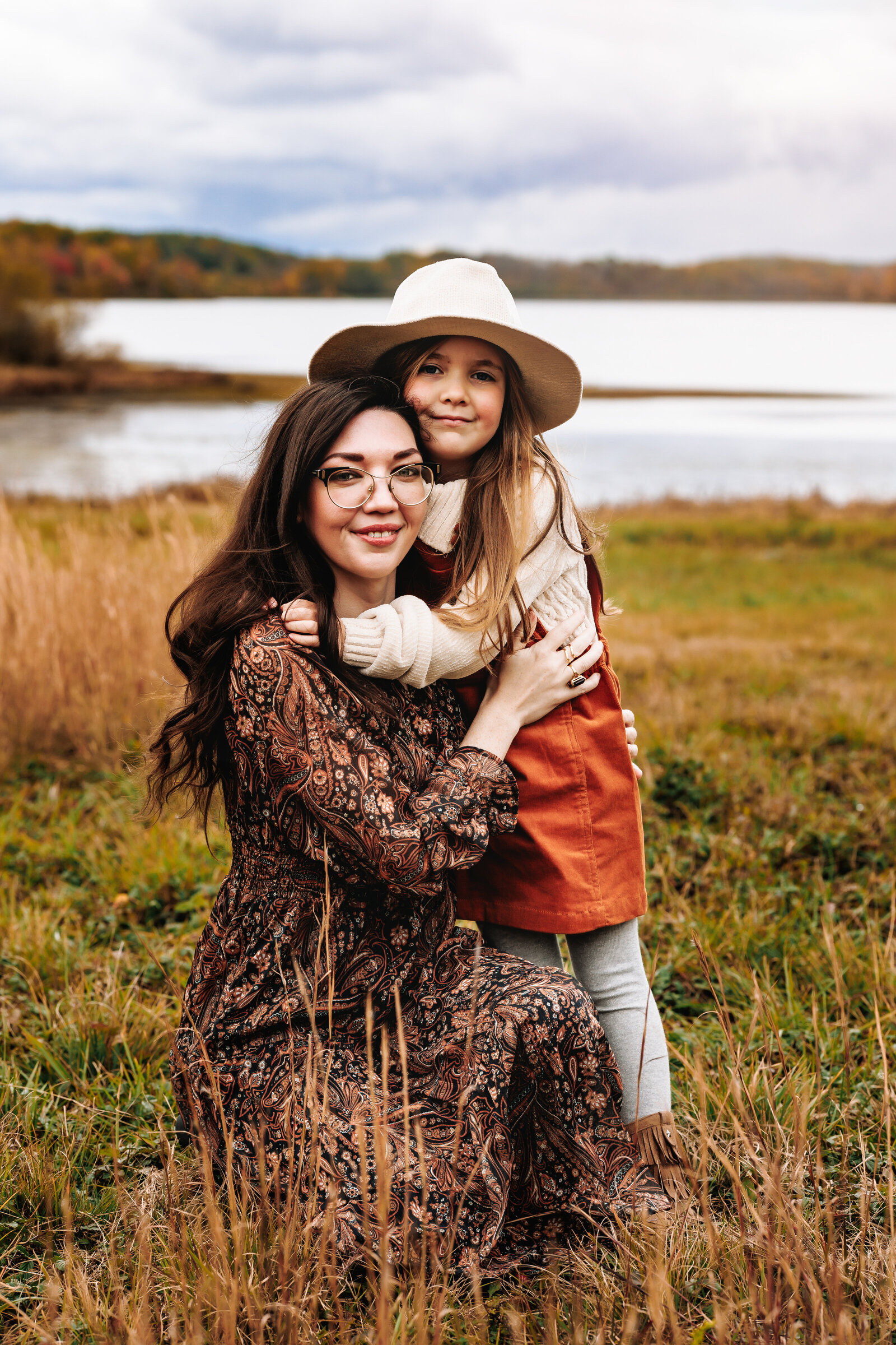 Mother and daughter snuggle up on a warm fall day near a small body of water