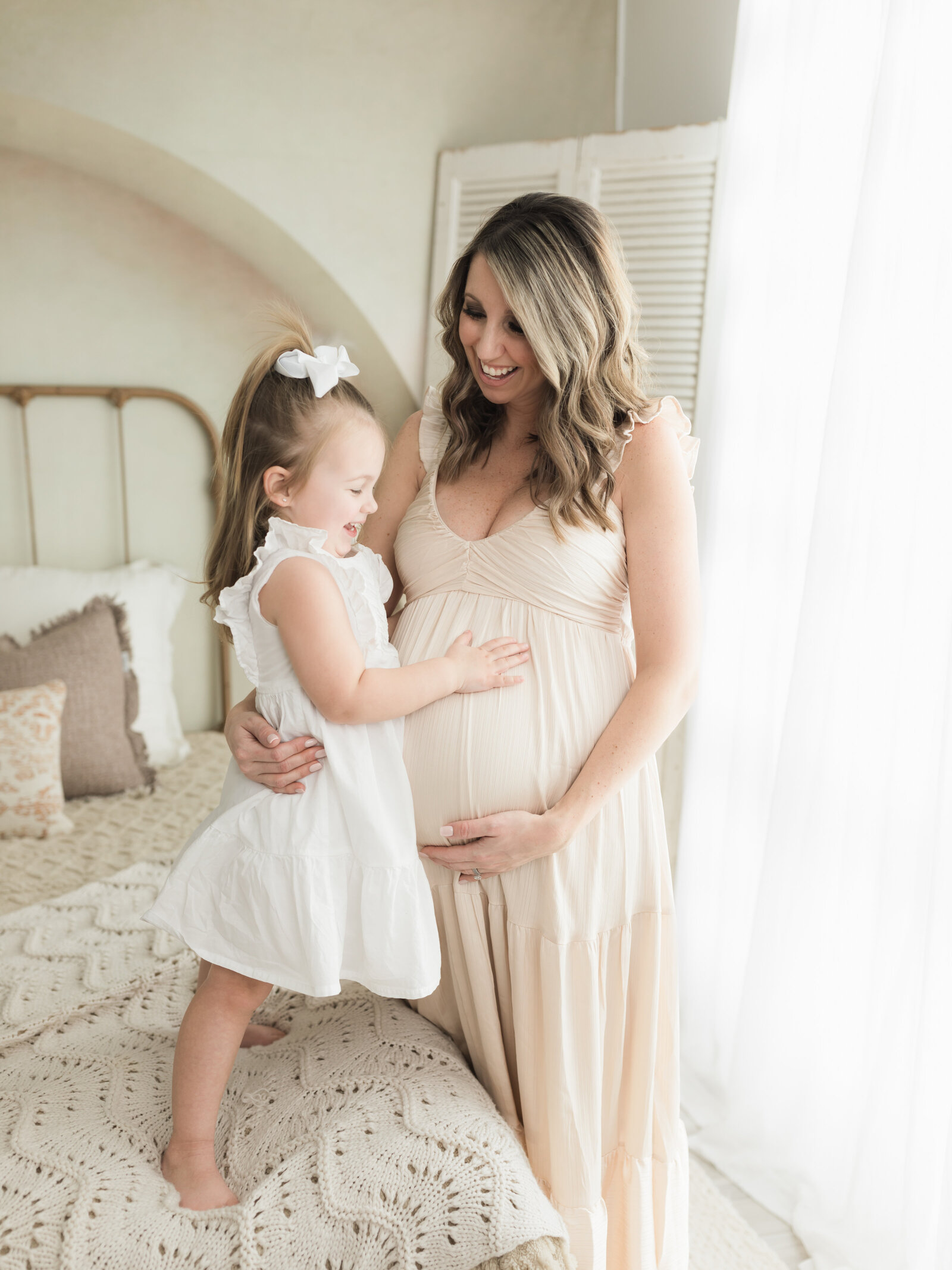 pregnant mother in cream maternity gown and daughter holding baby bump for maternity photoshoot cleveland maternity photographer