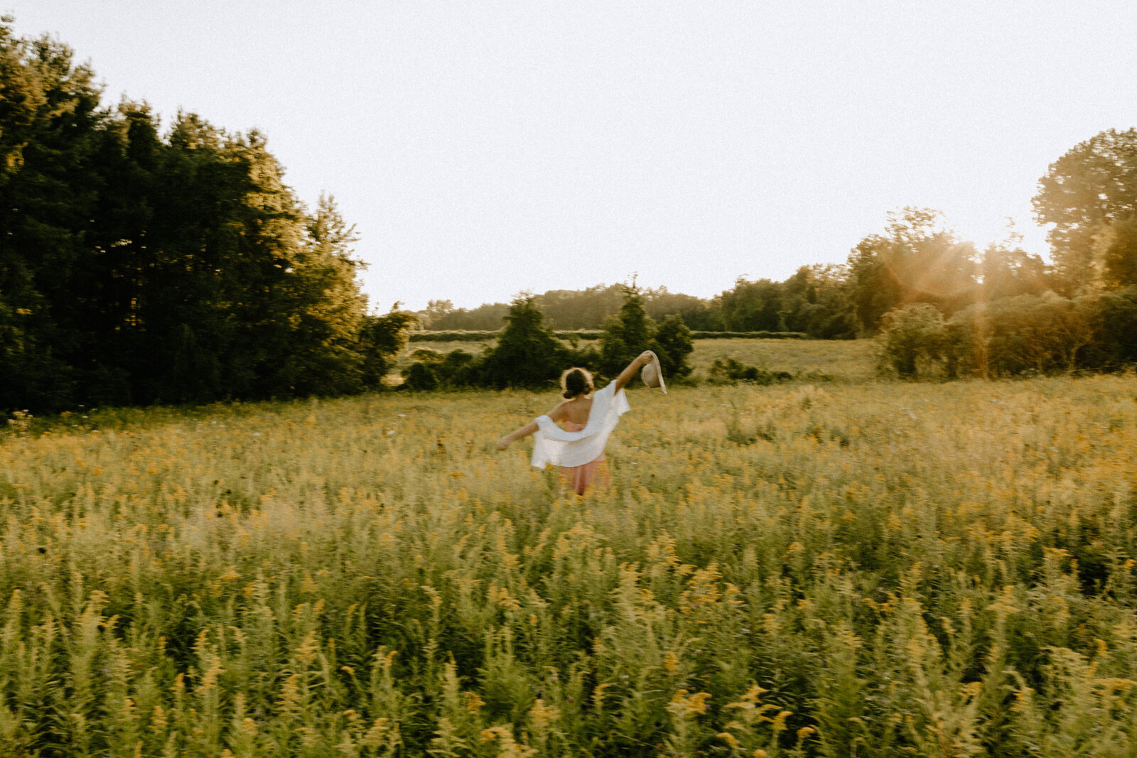 A girl standing in the middle of a big yellow field and splaying her arms out wide