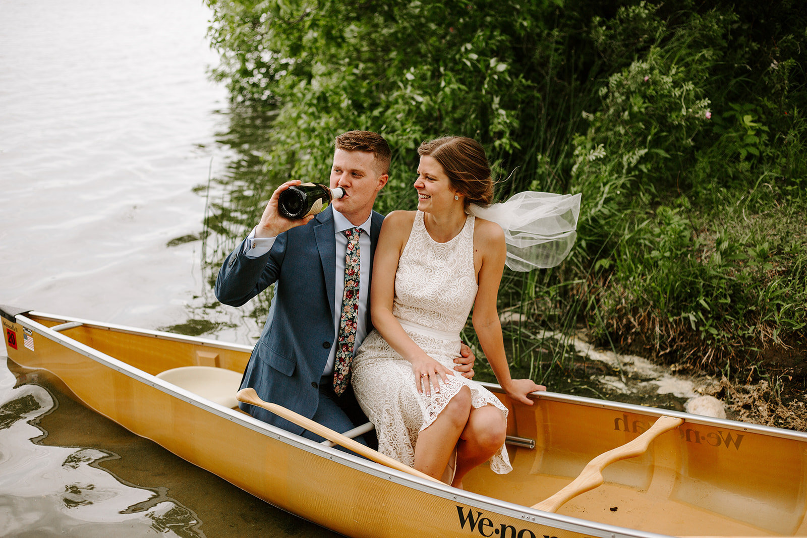 A couple drinking champagne in a canoe during their wedding elopement