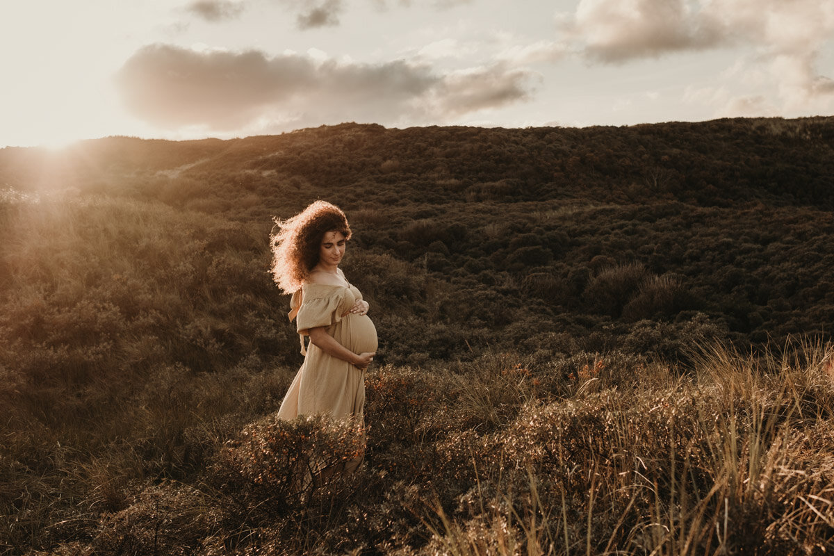 zwangere vrouw met wind door de haren tijdens zonsondergang