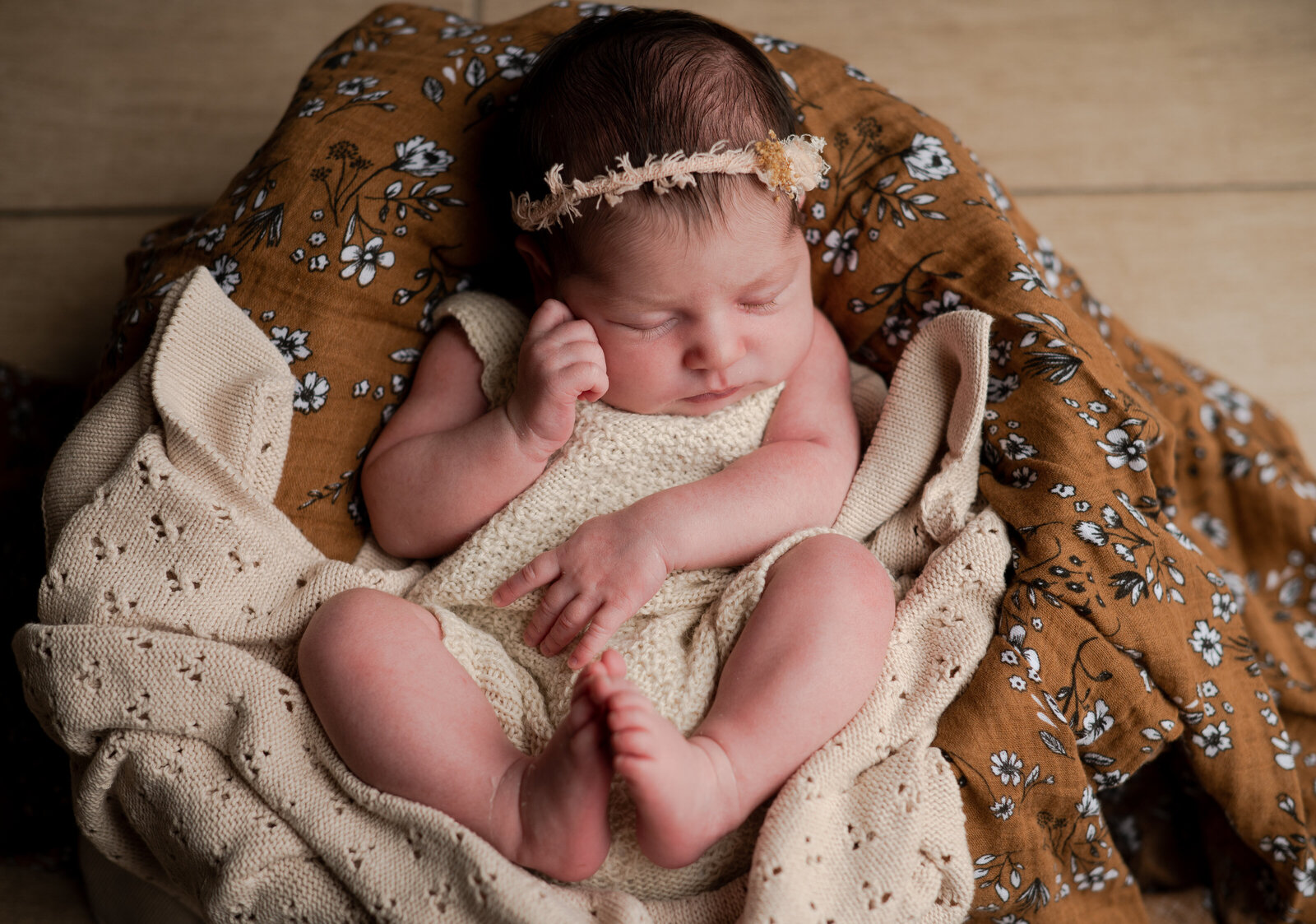 Newbaby baby sleeping in a basket on a brown floral swaddle.