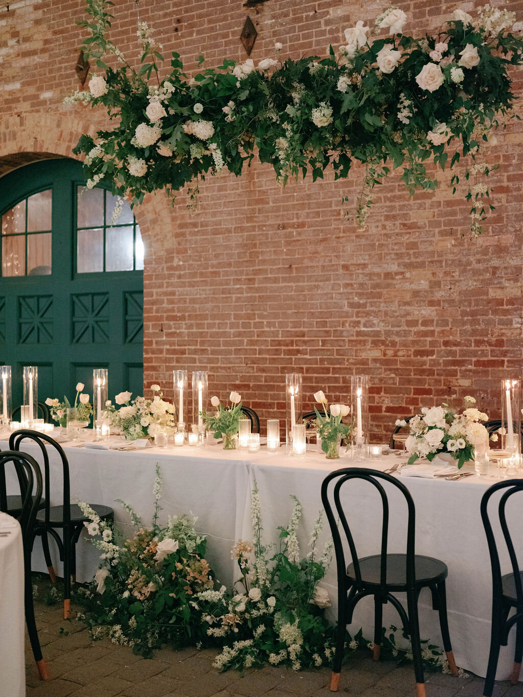 Lush greenery overhead structure hanging installation with white floral accents suspended above the head table in the Evergreen Museum Carriage House reception