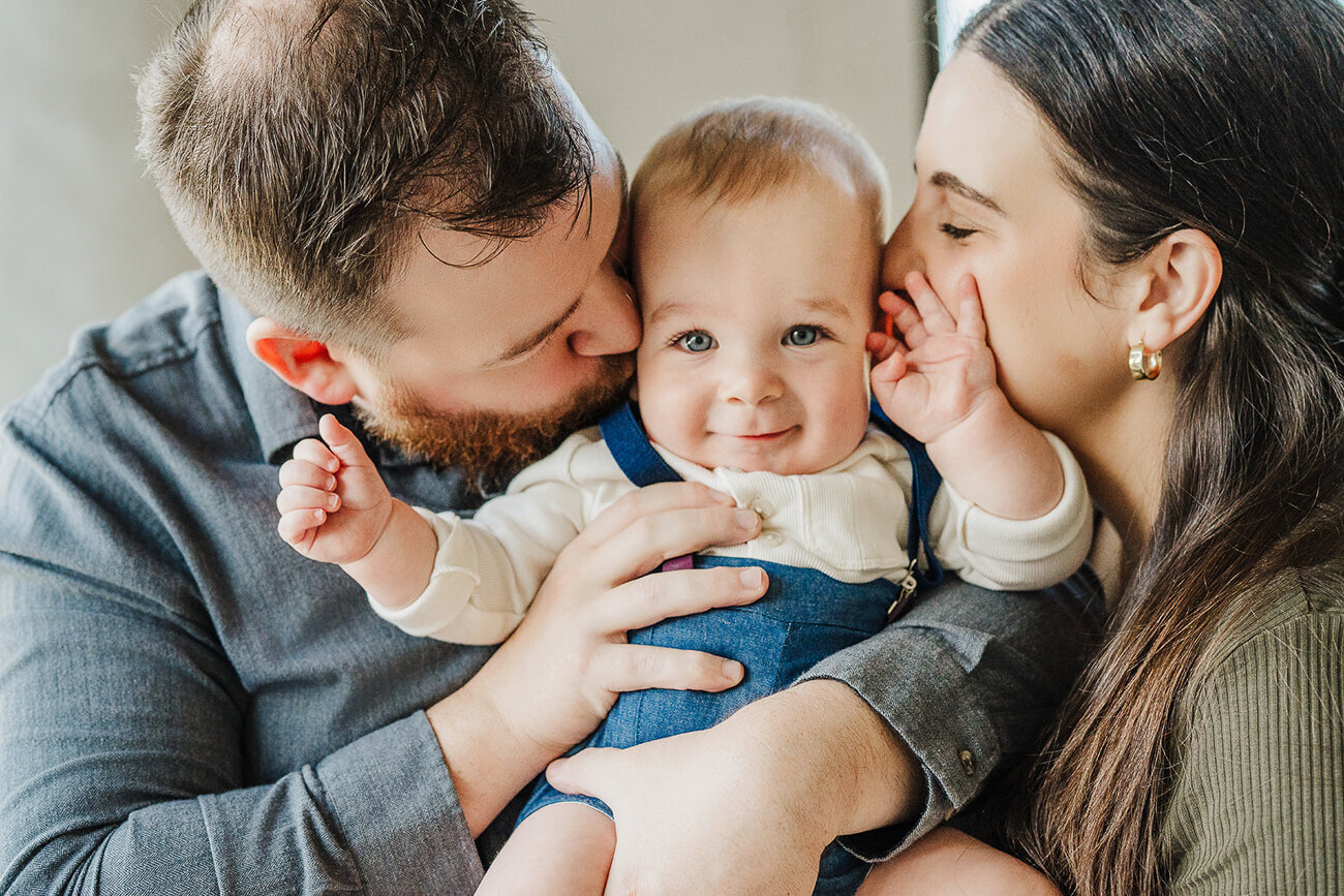 parents kiss cheeks of baby boy