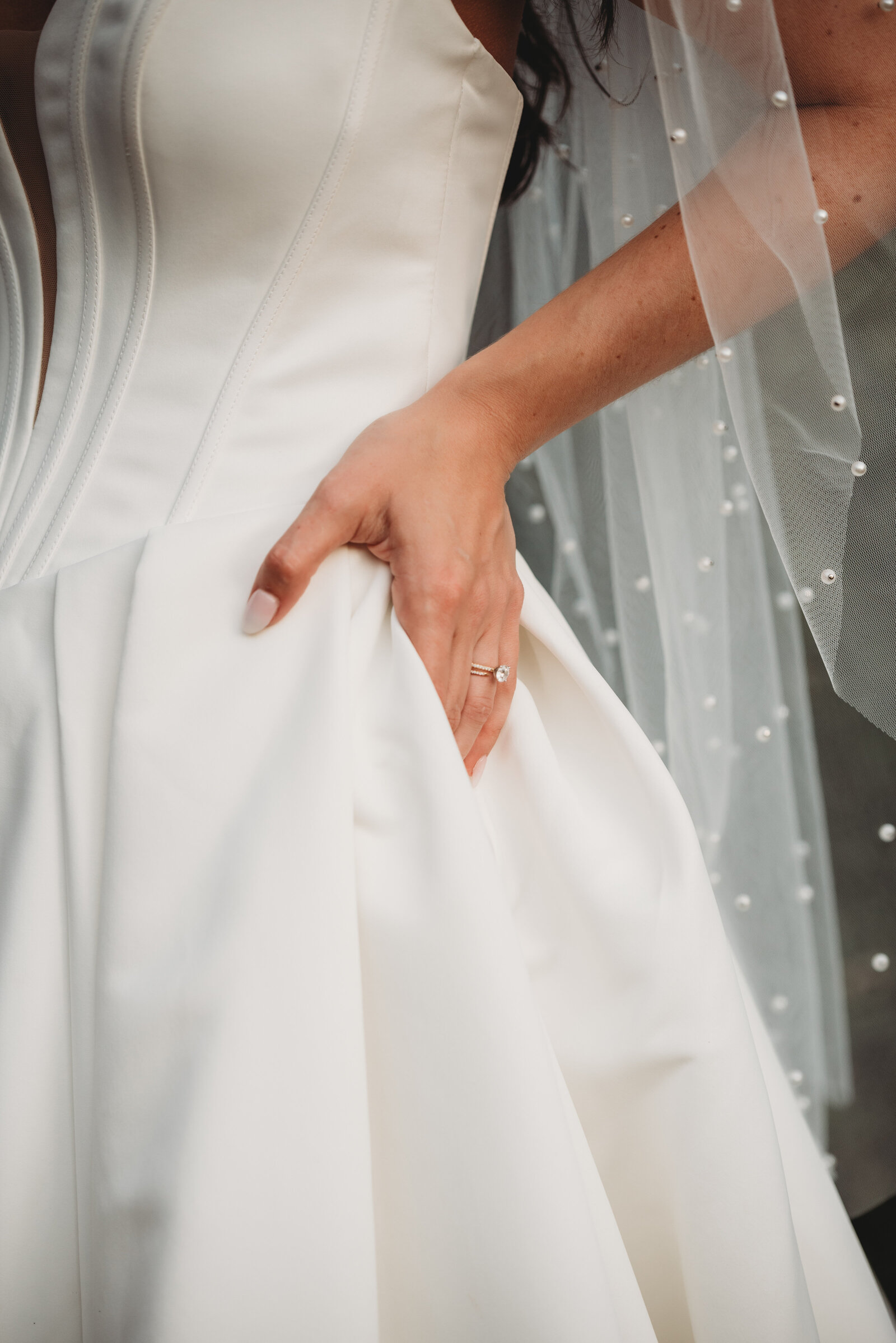 A stunning close-up of a bride’s wedding dress, featuring intricate fabric details, a delicate engagement ring, and a pearl-accented veil. This timeless bridal portrait captures the elegance and grace of a wedding day. Perfect inspiration for modern brides and luxury wedding photography in Connecticut.