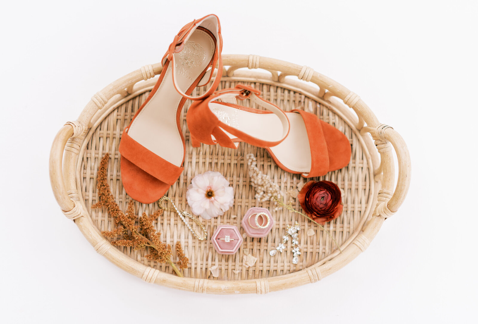 Portrait of orange heels, a blush jewelry box with engagement, ring, and earrings atop a rattan basket with flowers.