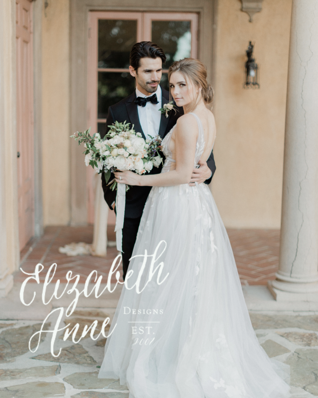 Kohnur fine art bride in a dreamy floral gown with natural, glowing makeup and soft, pinned updo embracing her groom in a romantic Italian-inspired villa featured on Elizabeth Anne Designs.