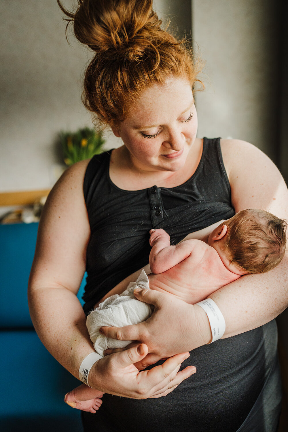 mom in black tank top nurses new baby in hospital after birth
