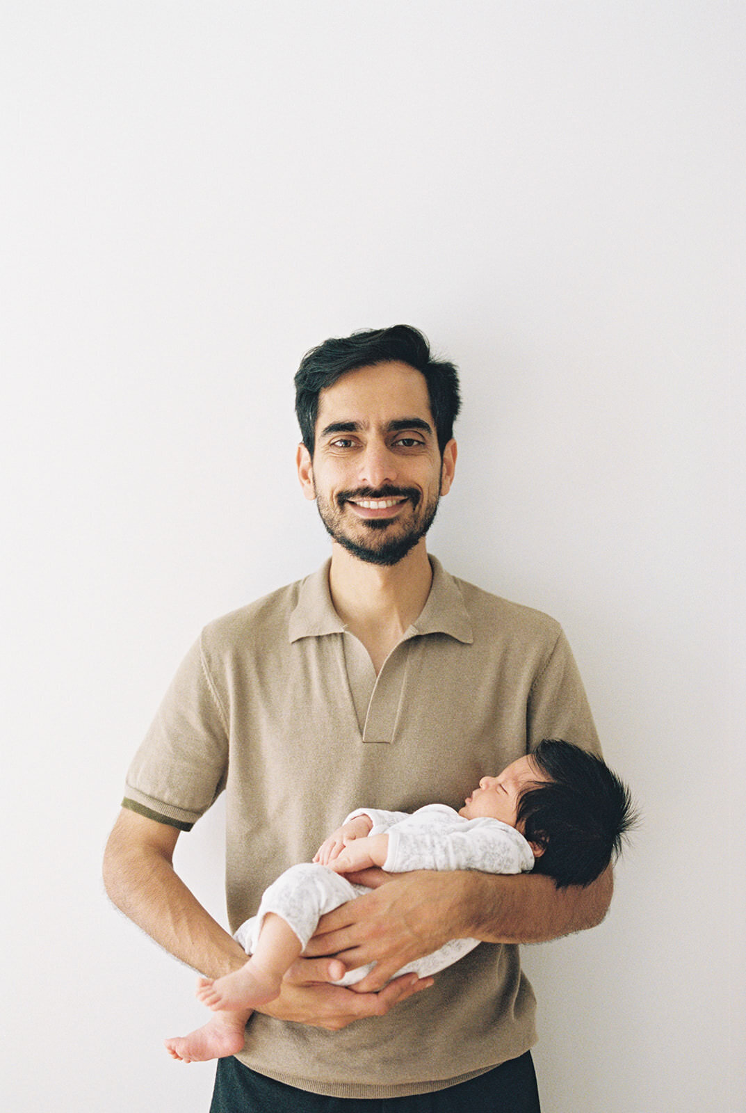 Proud father holding his newborn baby against a minimal white backdrop