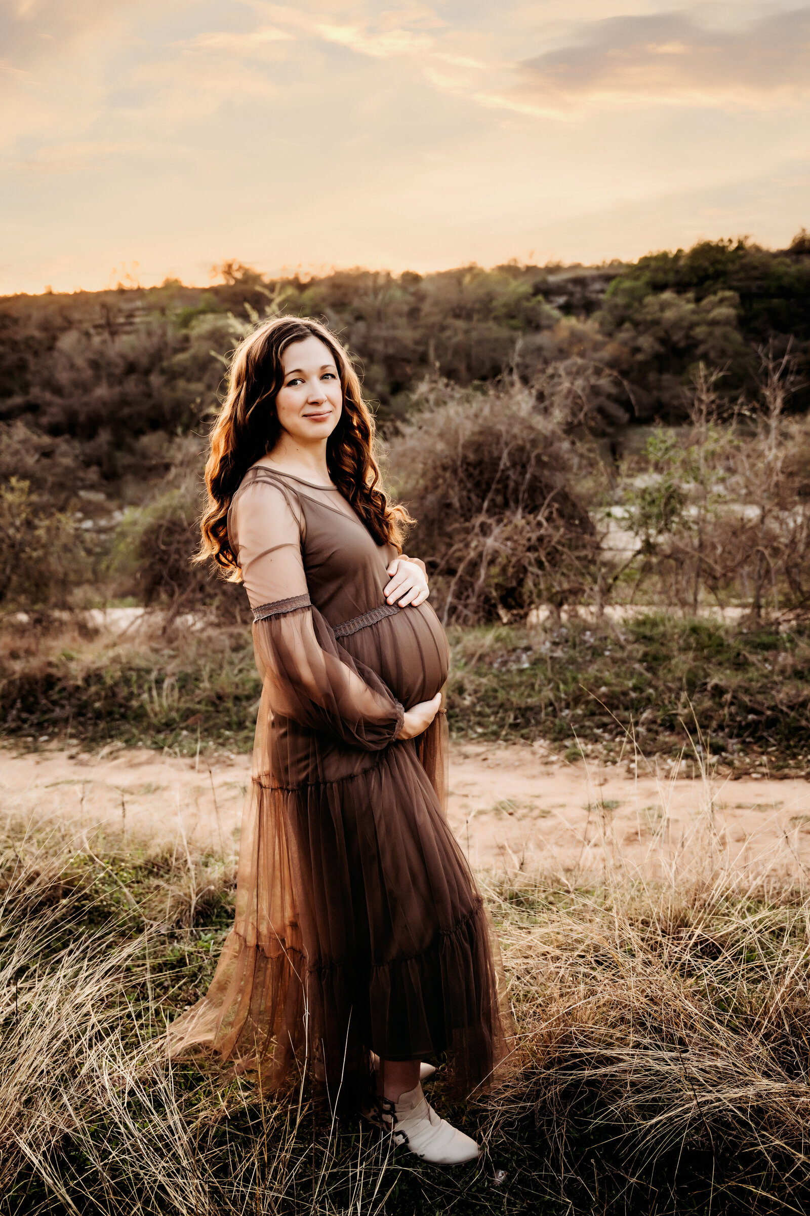 Maternity Photographer, an expectant mother supports her pregnant belly as she walks in a field