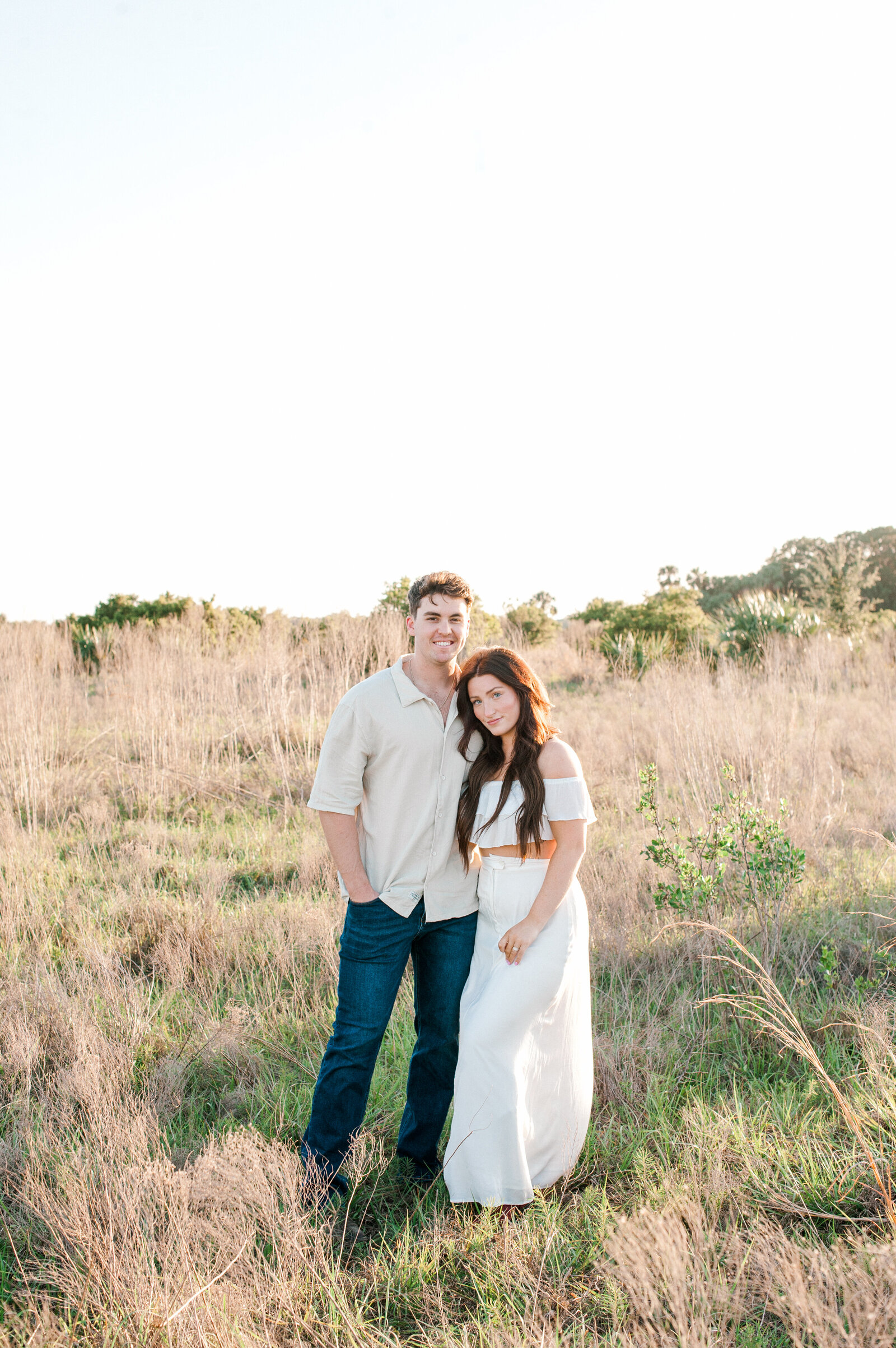 Portrait of a couple standing in a tall grass field smiling at the camera