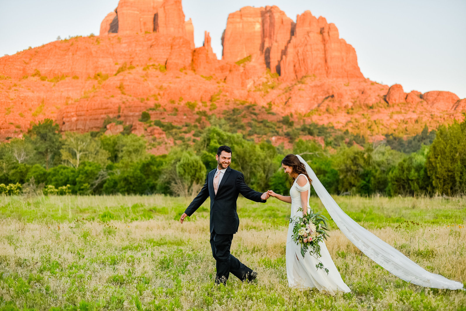 Sedona Crescent Moon Ranch wedding couple bride and groom walking in green field Cathedral Rock behind