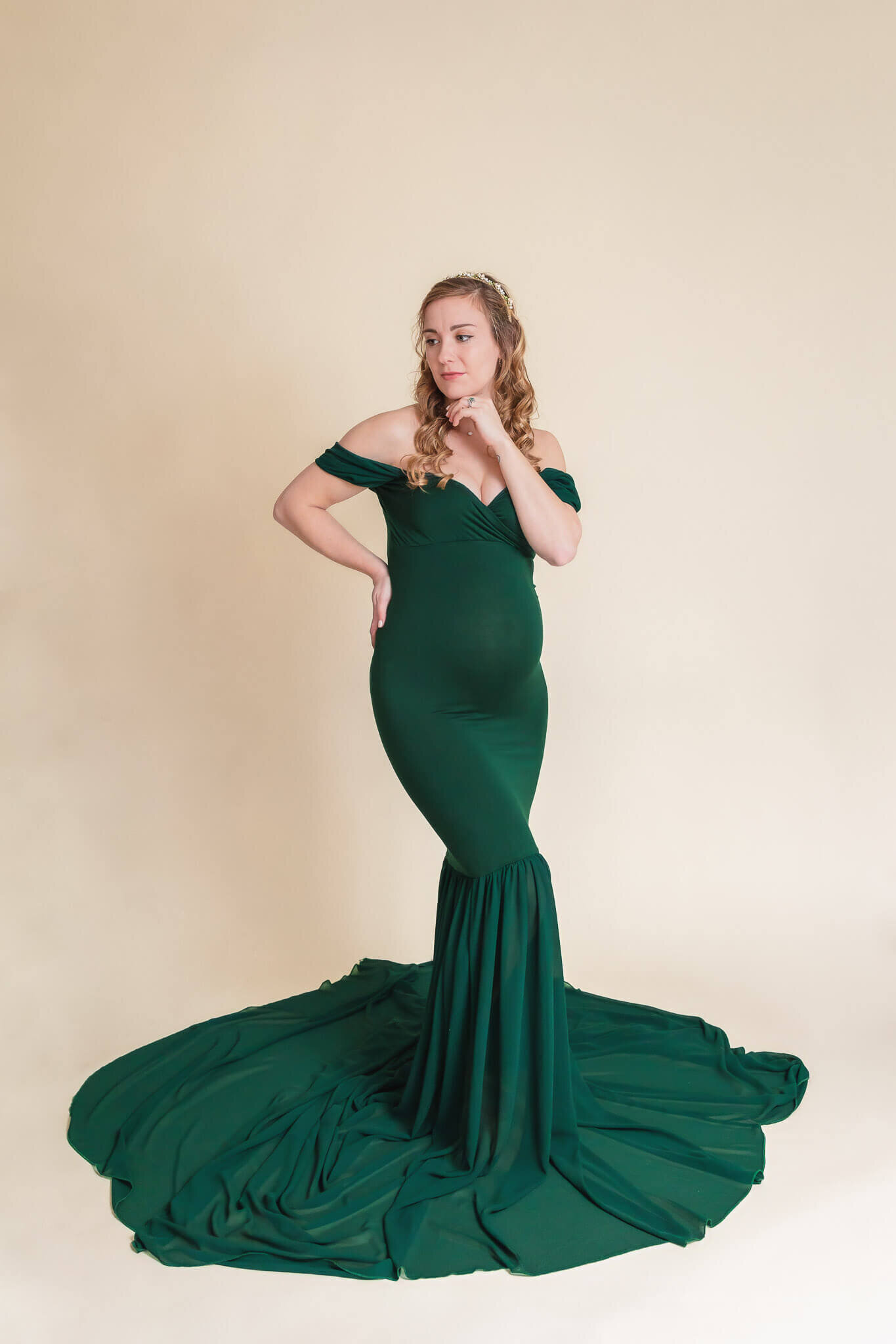 A pregnant woman in a green dress posing on a cream backdrop in a Gainesville studio.