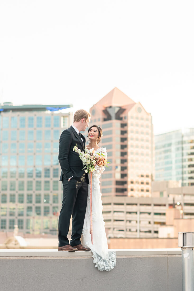 A bride and a groom stand together with the tall buildings of downtown Salt Lake City in the background. Captured by Melissa Woodruff Photography