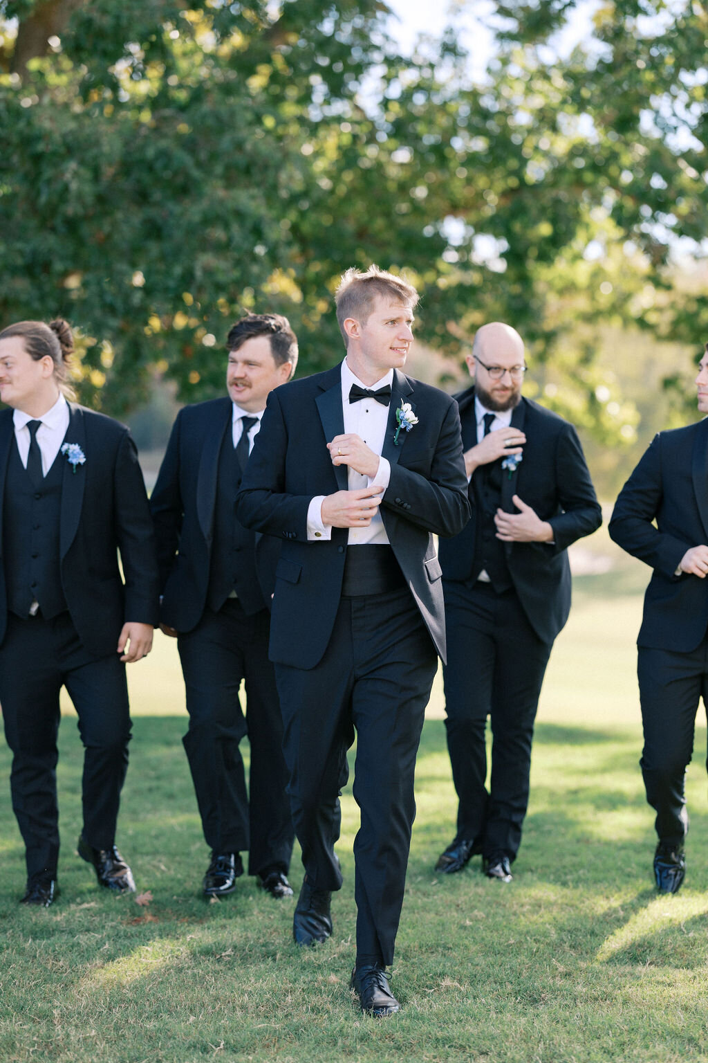 Groom adjusts cufflinks with groomsmen behind him at Chimney Oaks