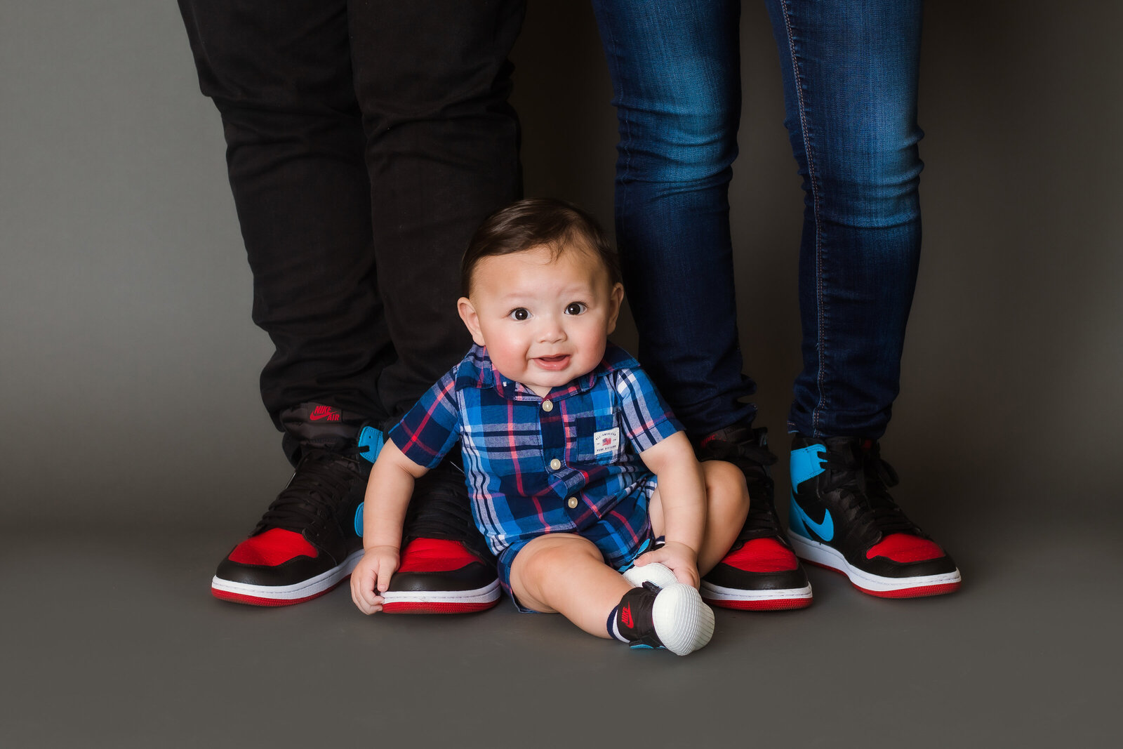 Milstone Photographer, a baby sits at his parents feet, they both wear matching sneakers