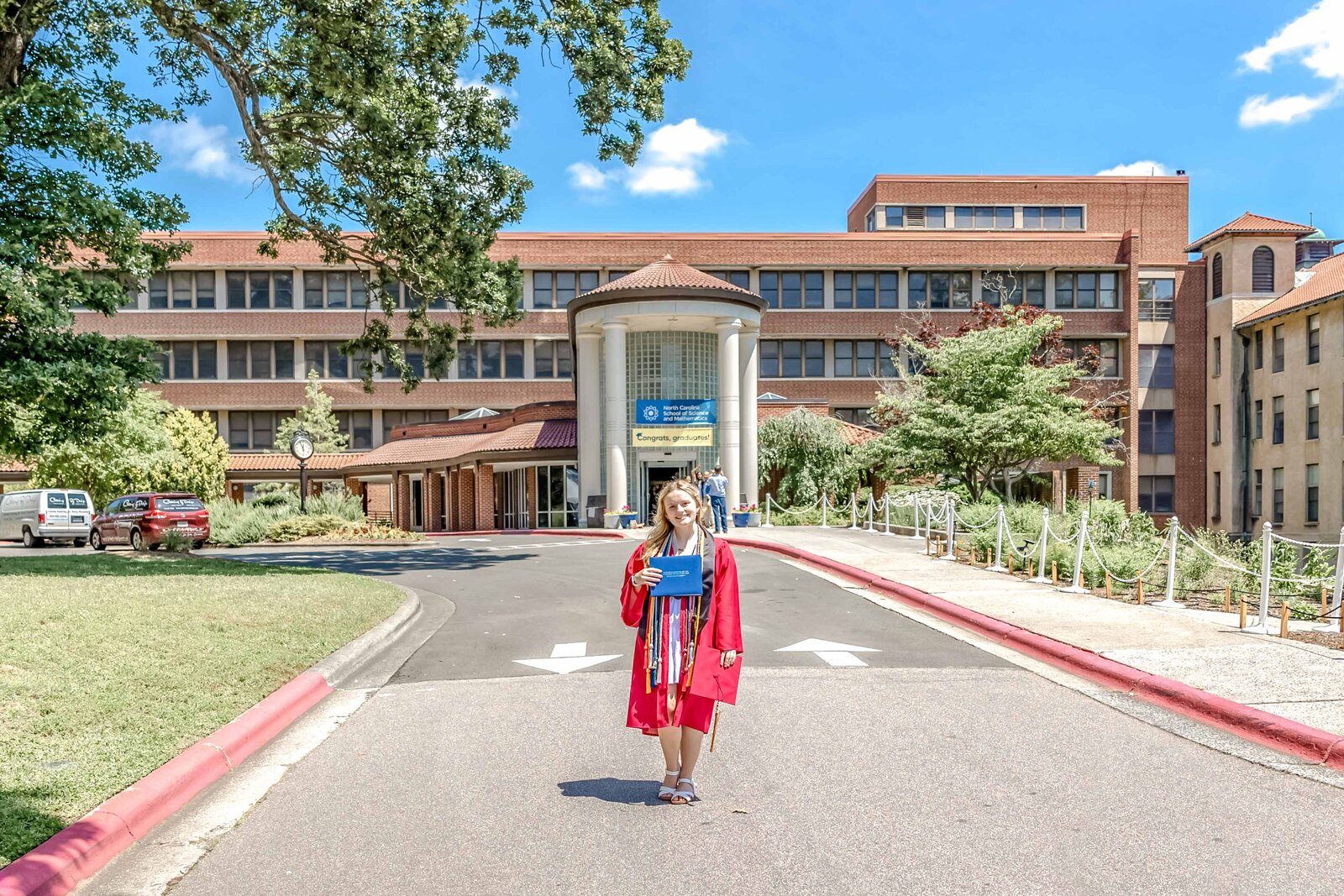 A high school senior in a red cap and gown standing proudly in front of North Carolina School of Science and Math in Durham, North Carolina. This portrait captures the excitement of graduation, ideal for those seeking meaningful and professional senior photography.