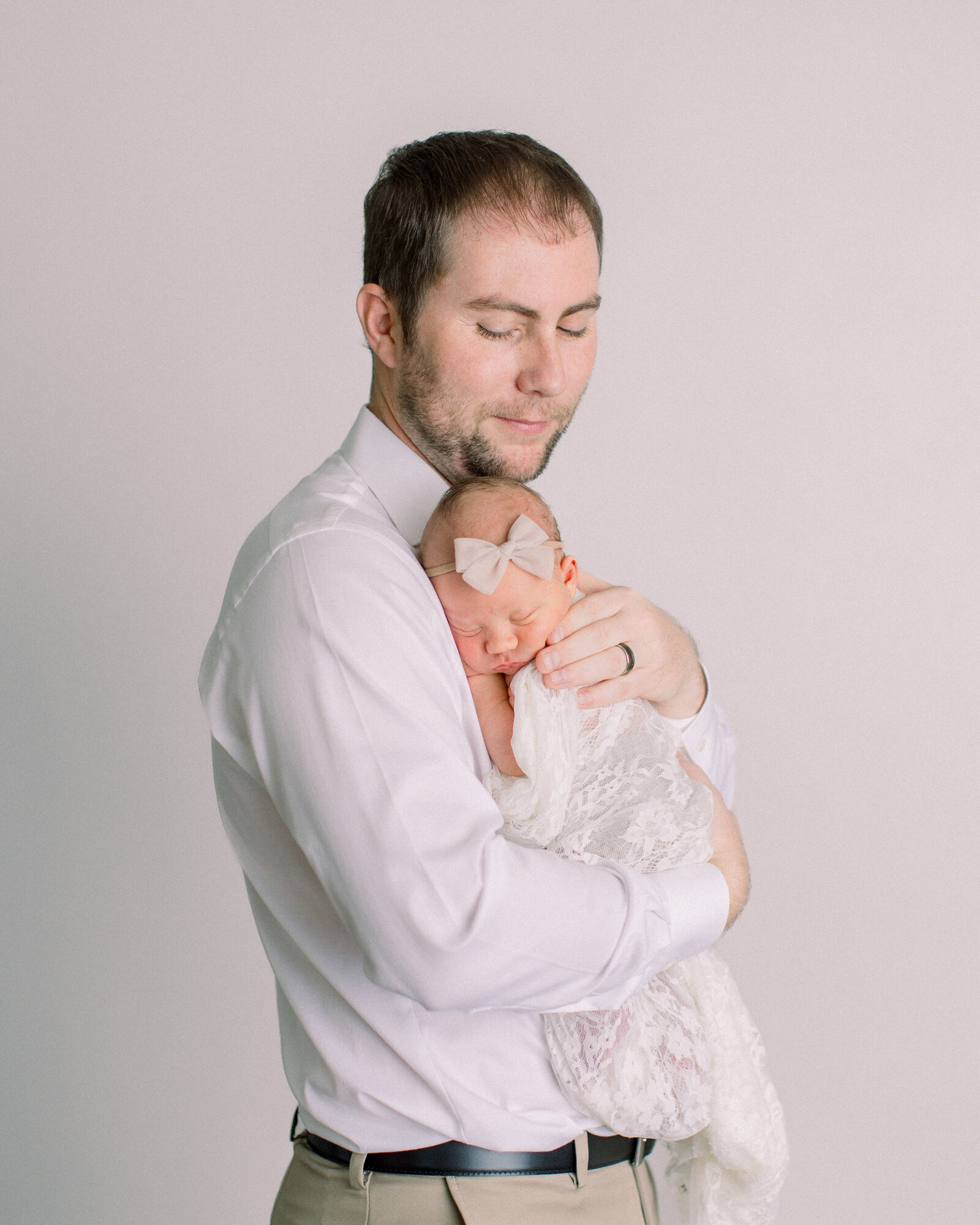 New Dad snuggles his sleeping baby in a neutral studio by NH newborn photographer Fieldstone Studio.