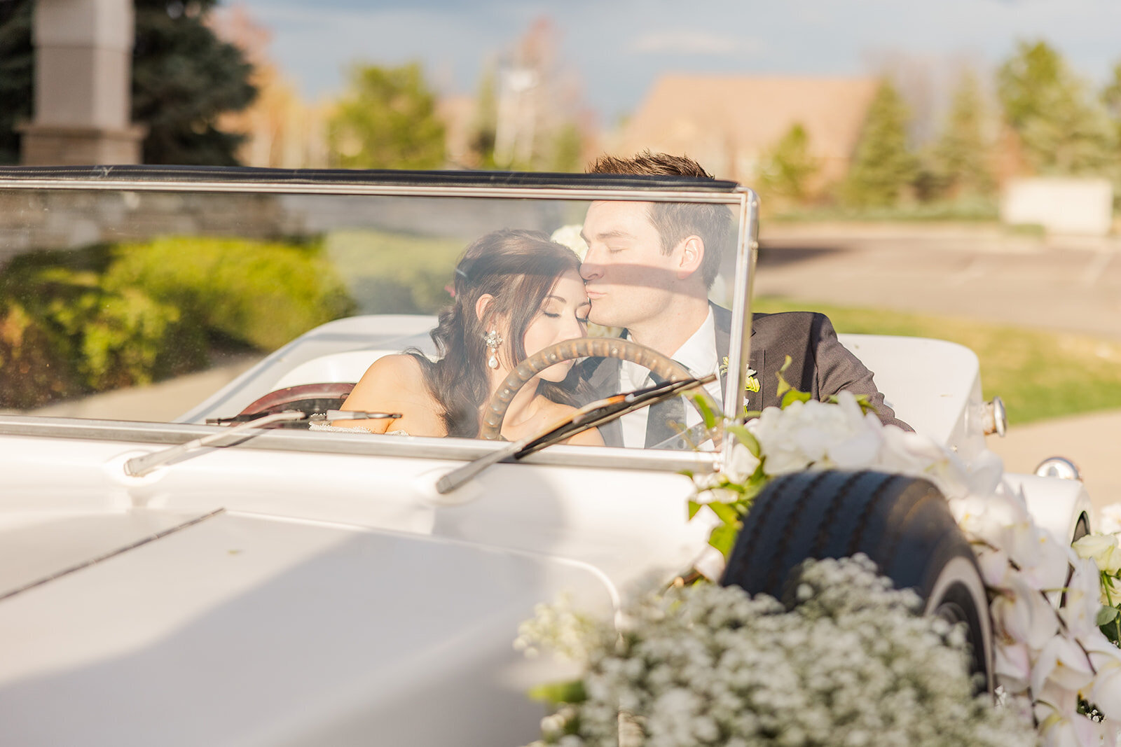 Bride and groom sharing an intimate moment together in an old fashioned car on their wedding day at the Chateaux on Fox Meadows in Broomfield, Colorado.