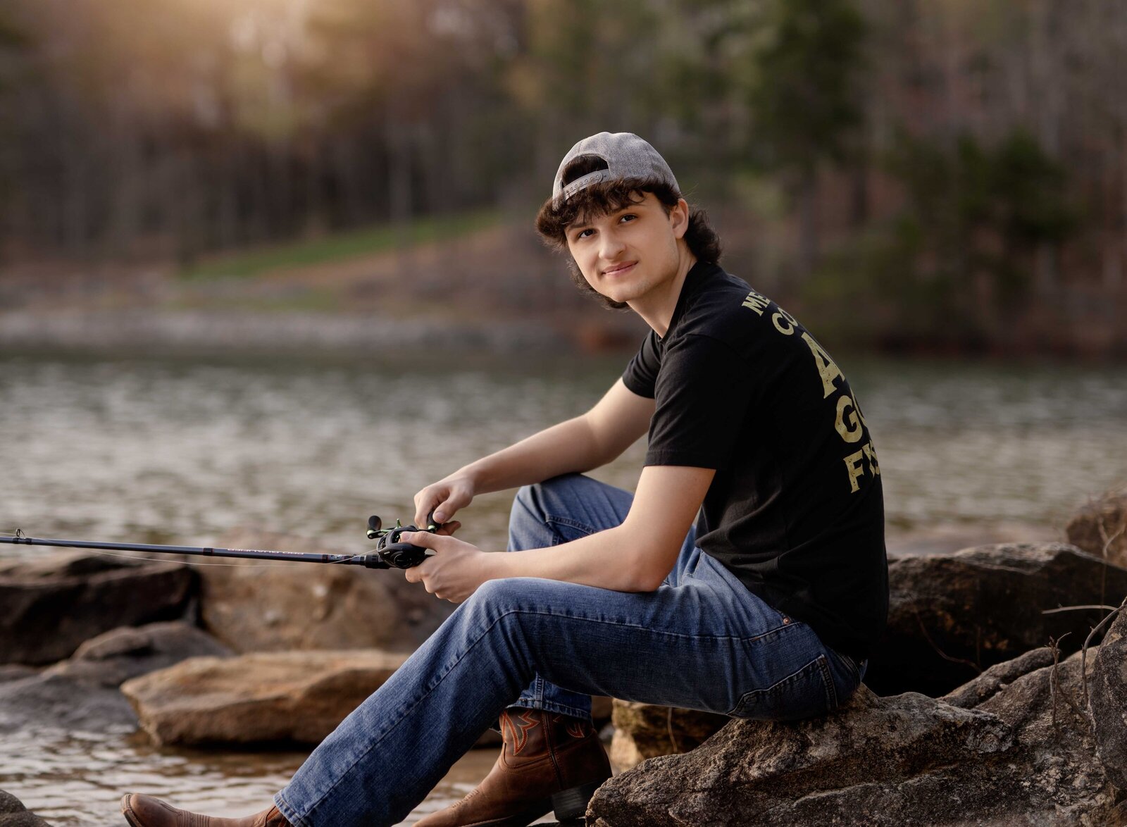 Boy sitting on rock at lake and fishing. Senior graduation photos taken by Jenni Nikki Photography in Atlanta, GA
