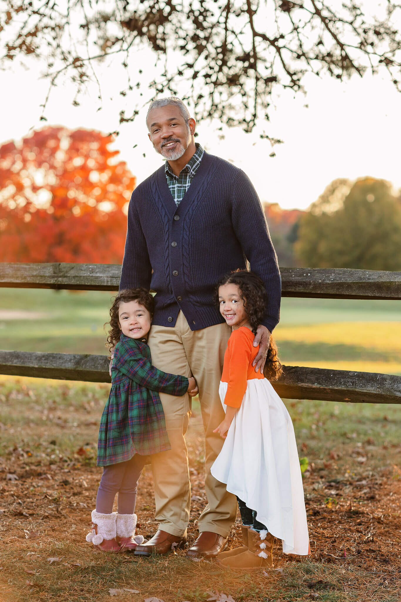 A dad standing against a fence with his two daughters