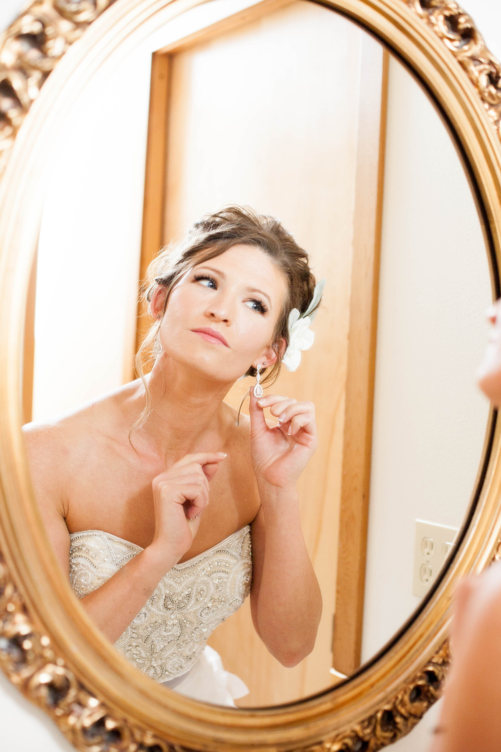A woman putting on earrings in a mirror.