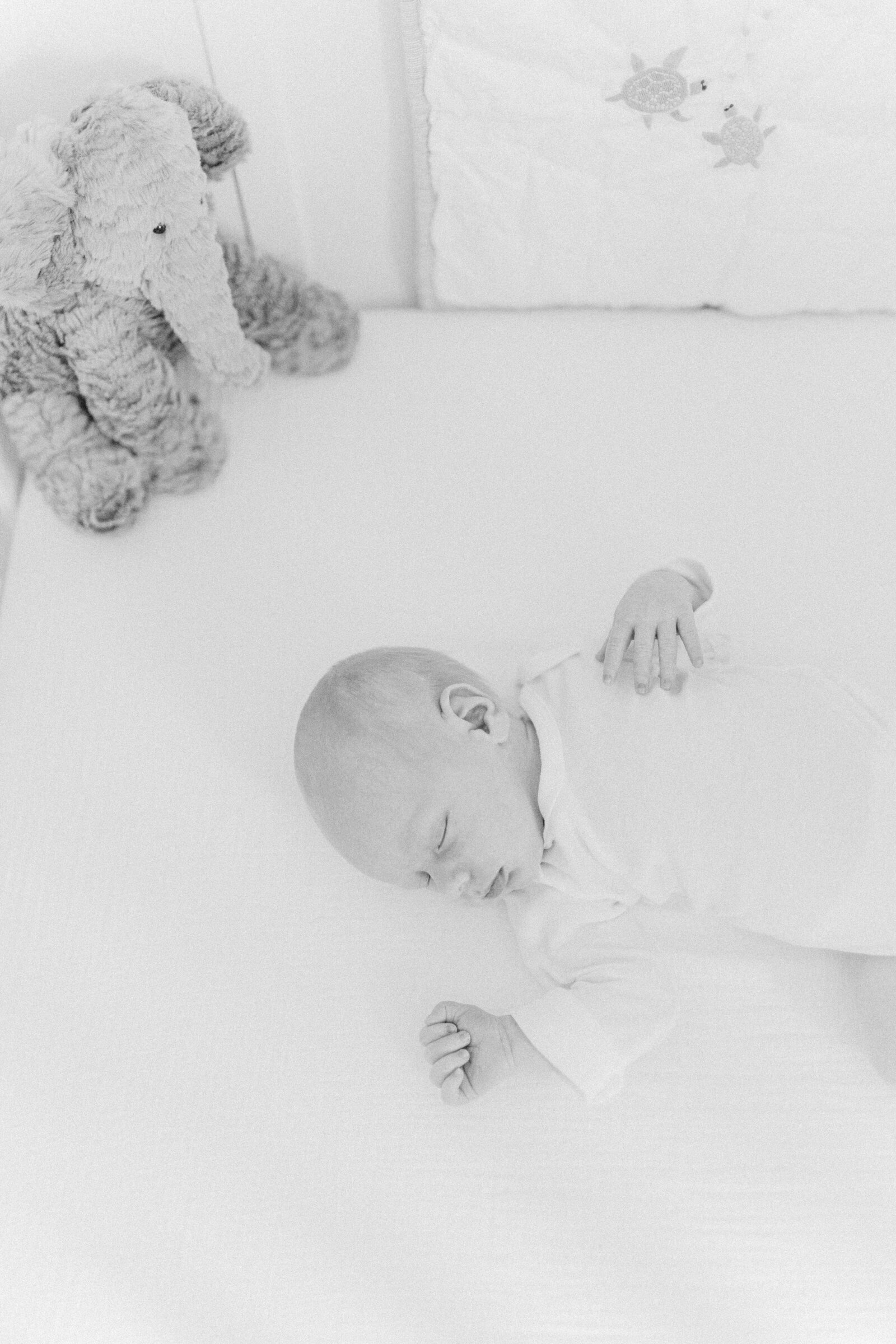 A black and white image of a newborn baby laying down in their crib
