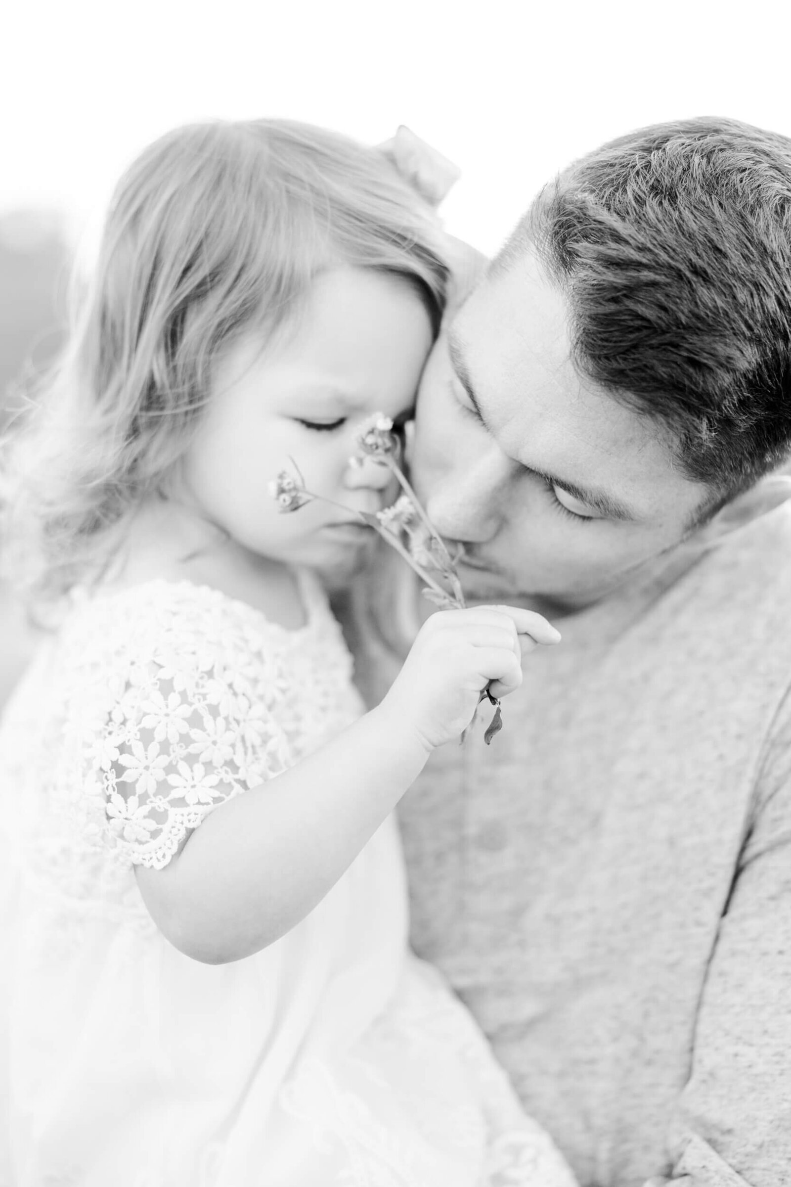 Black and white, dad holds his little girl and they smell a flower together