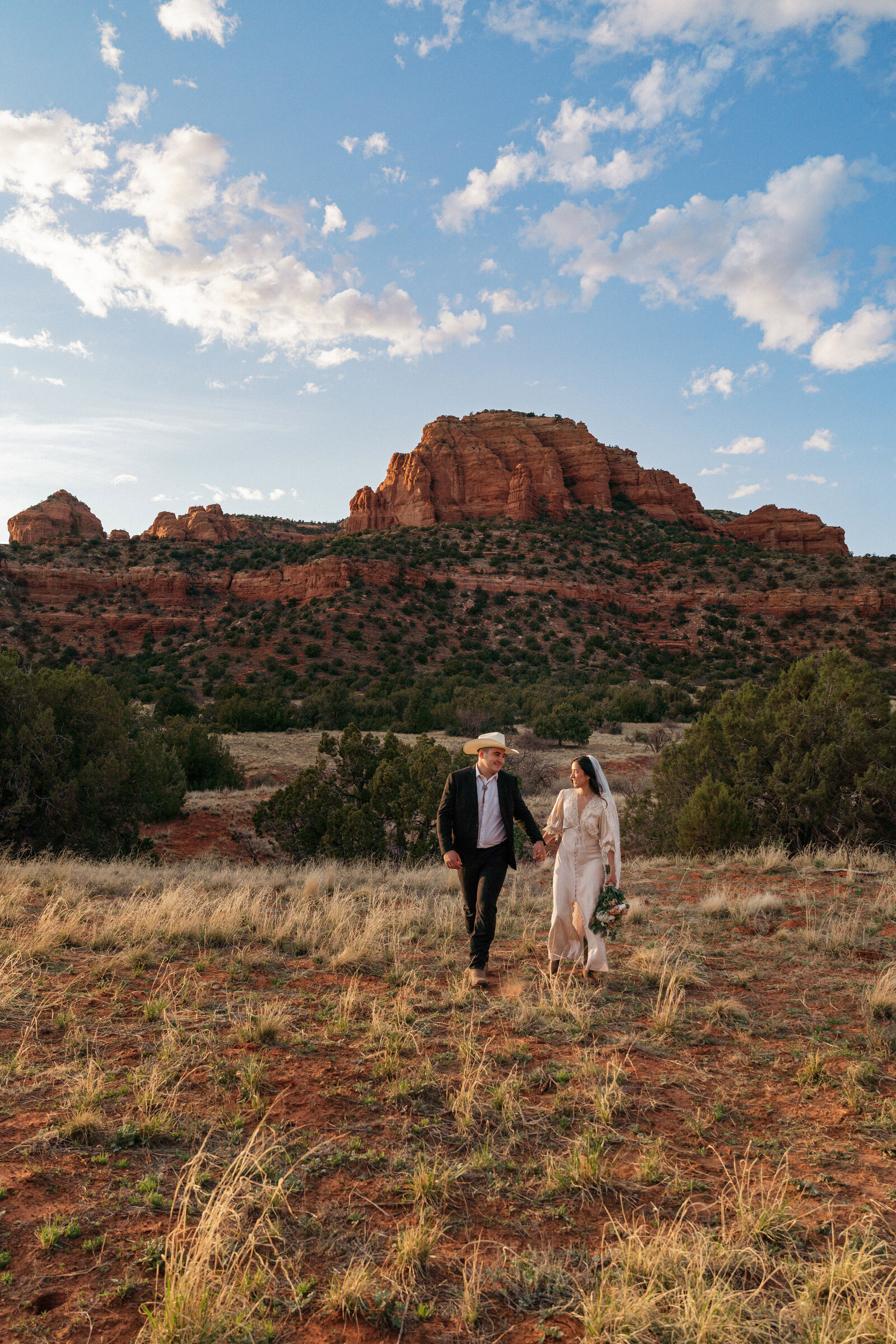 Bride and groom walking hand in hand through red rock desert landscape at Bear Mountain during their Sedona elopement.