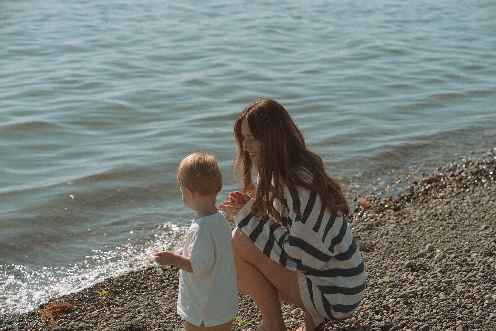 female wearing blue striped outfit playing on beach with son