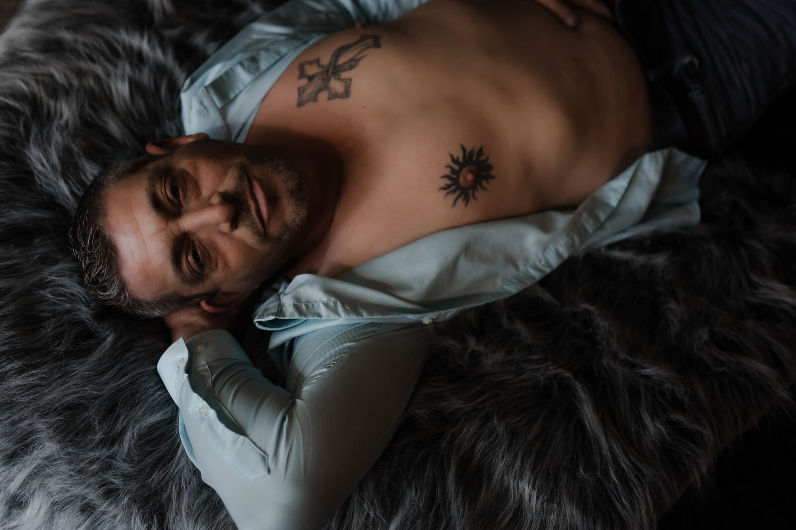 A man Smiles While laying on a bed in unbuttoned shirt