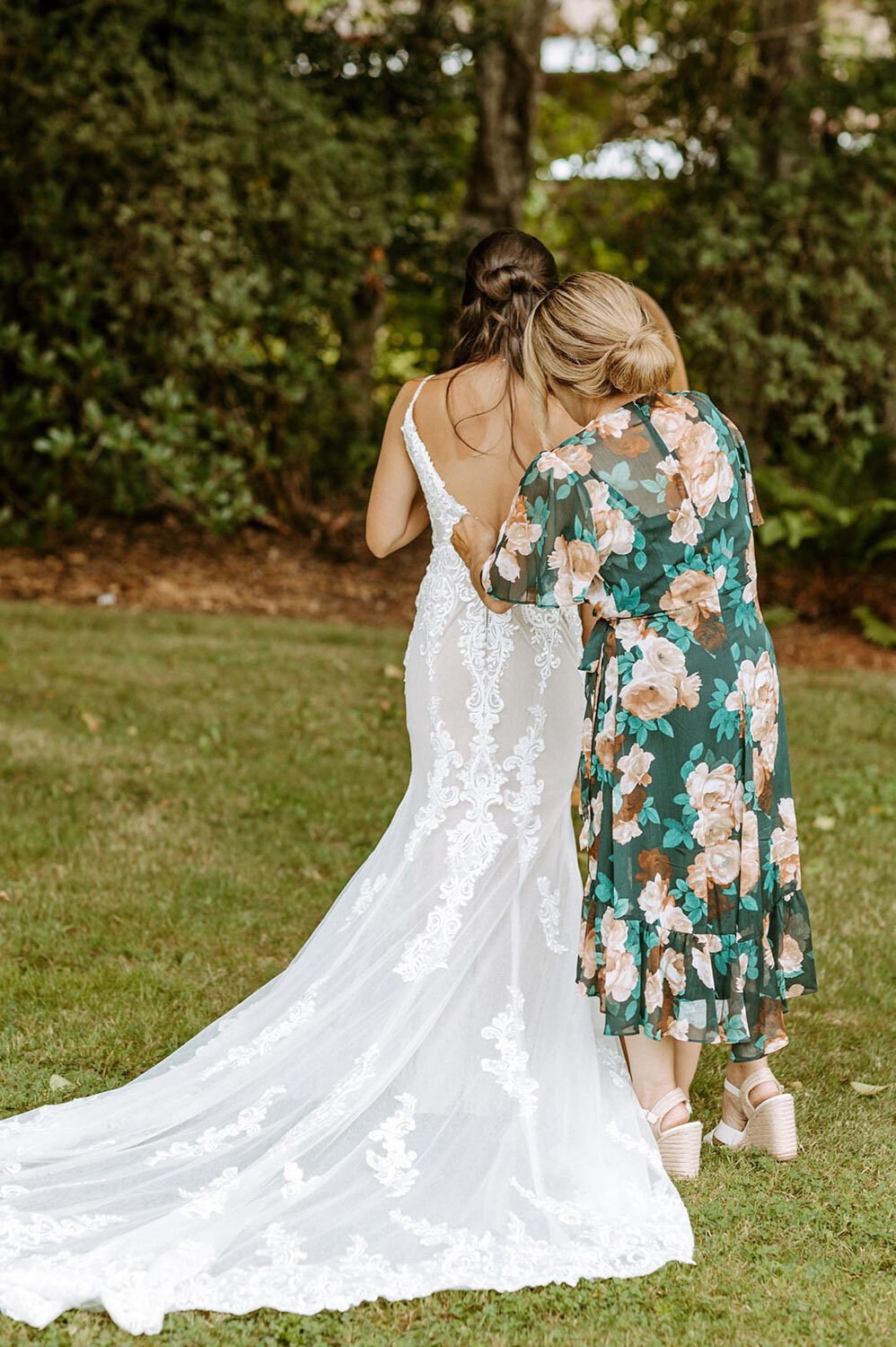 A loved one adjusting the bride's lace train in an outdoor setting