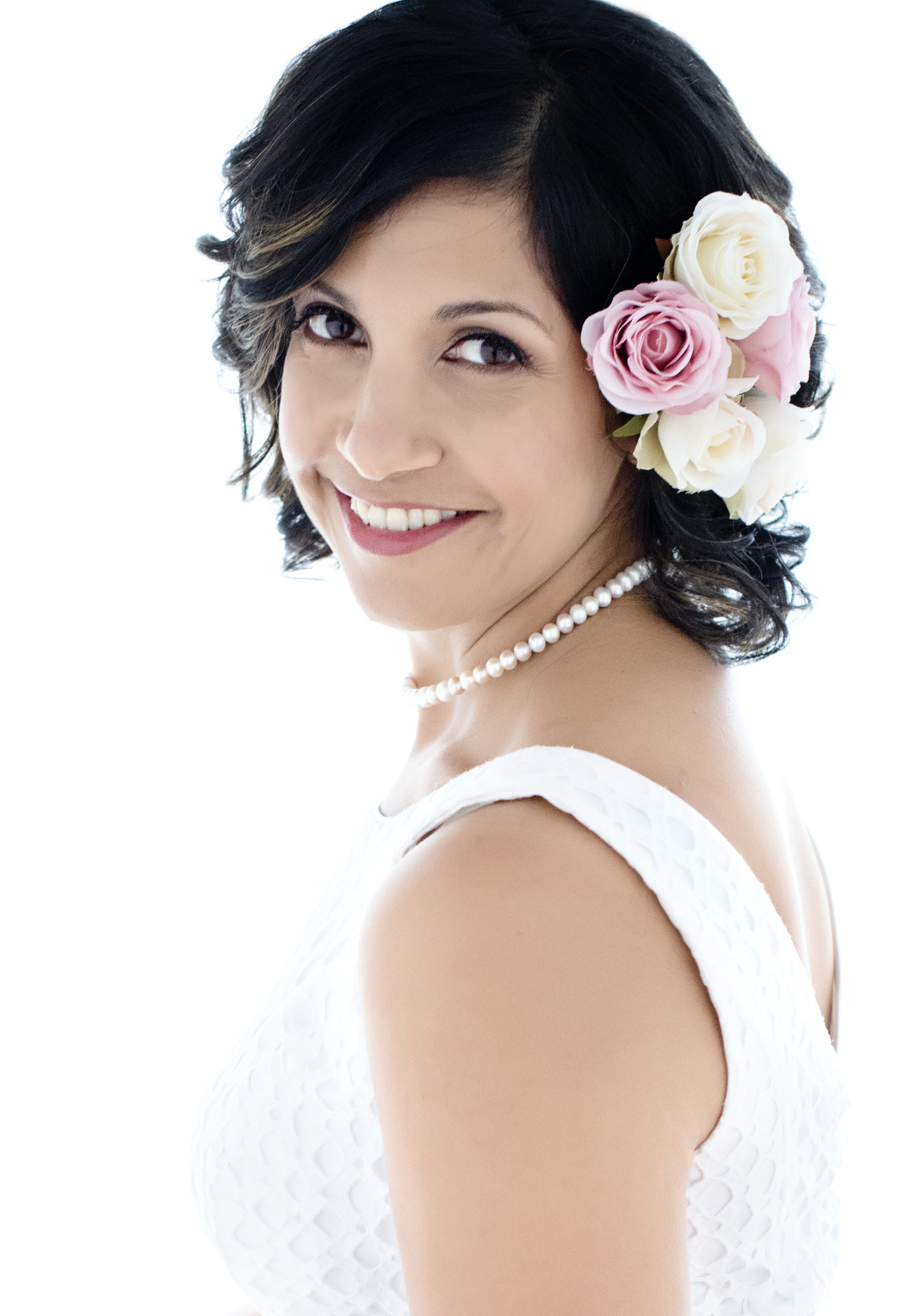 branding photo portrait of a woman looking in the camera and  smiling with  flowers in the hair and  pearl necklace  with  white dress and  curly short hairiness Branding, Headshots, Makeover Photoshoots in Mississauga, Oakville, Milton, Burlington, Toronto, GTA