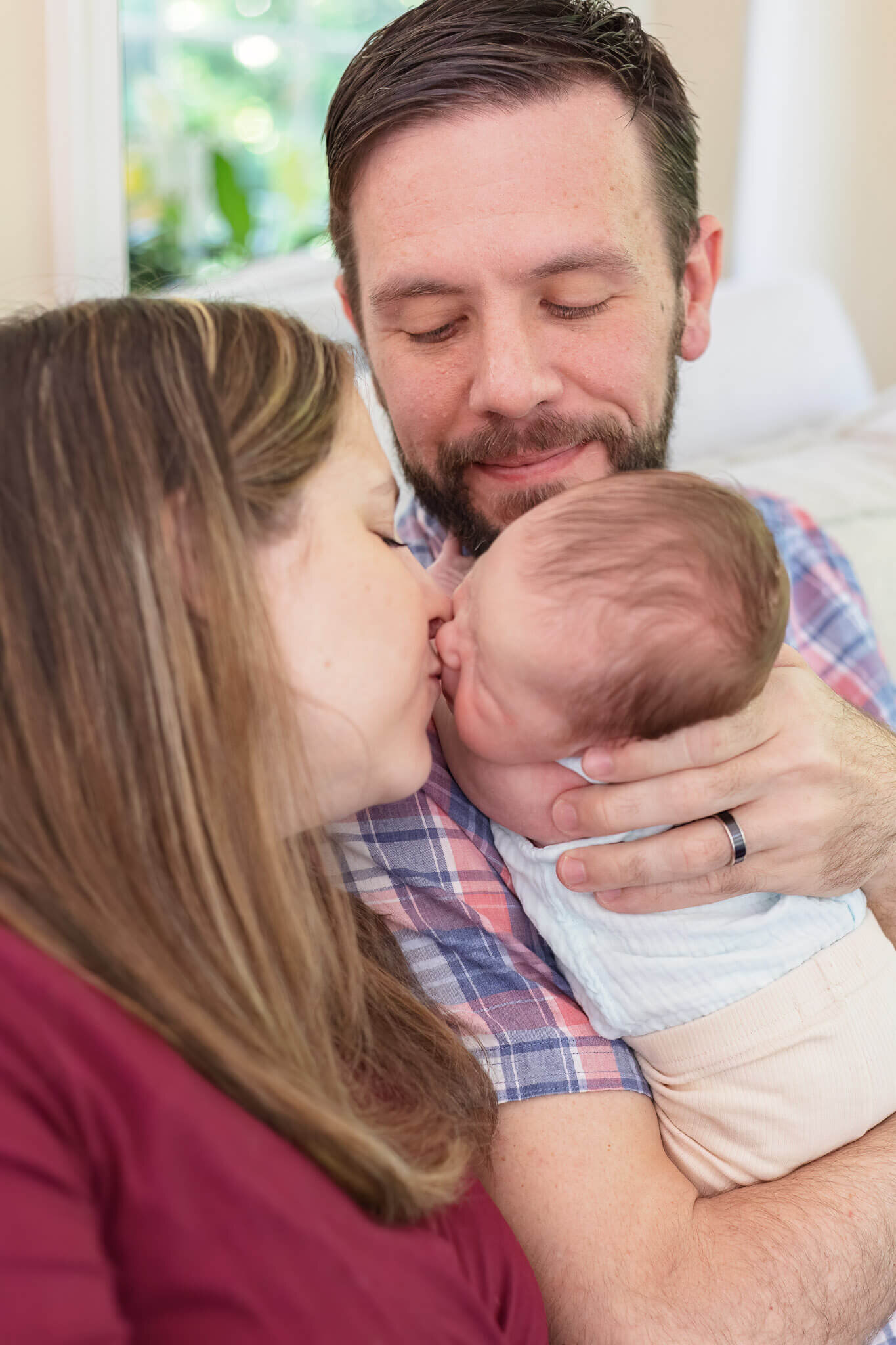 A mom kissing her newborn daughter while dad holds her.