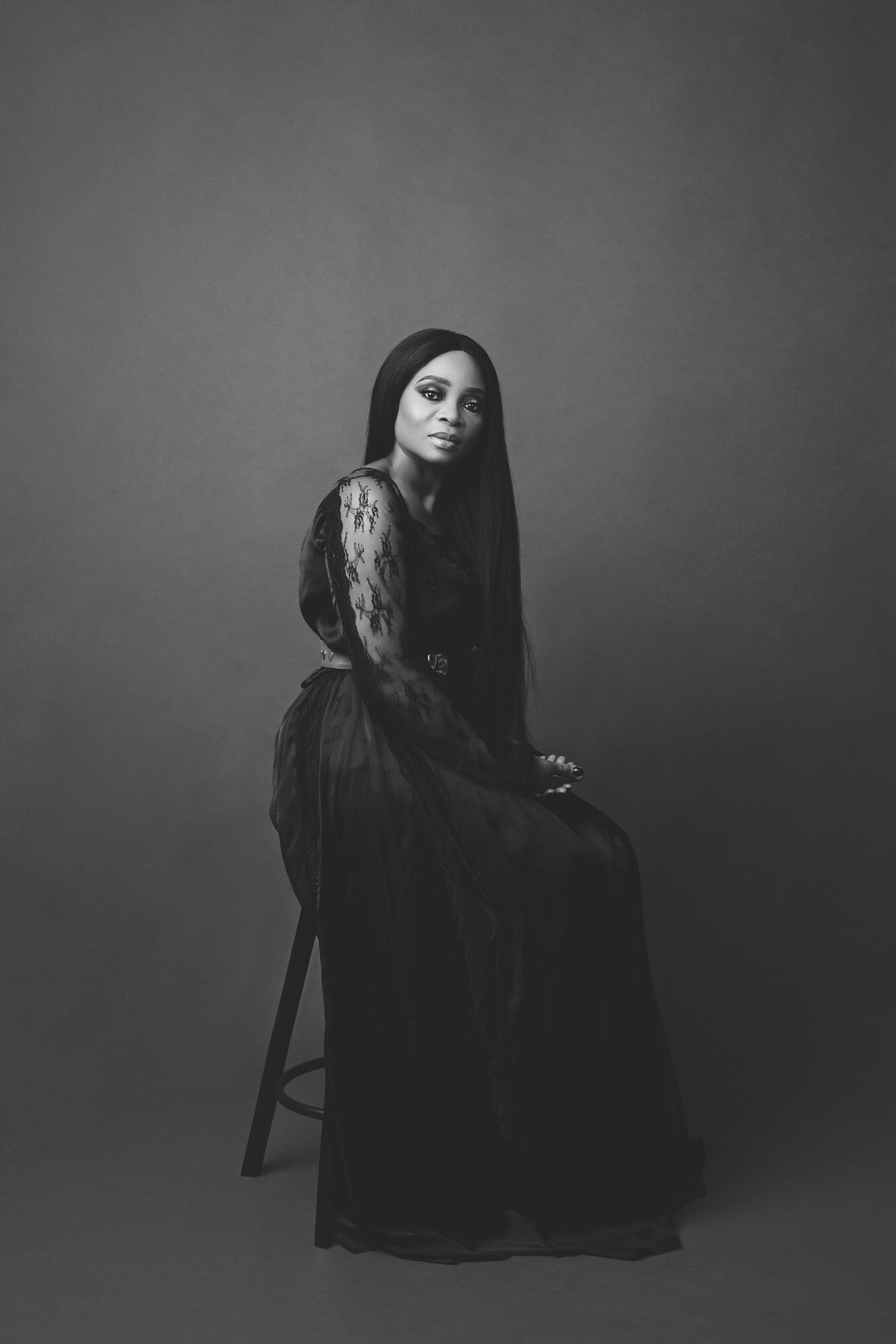 Black and white portrait of a woman in a black dress sitting on a stool, looking camera center.  Houston top-quality portraits.