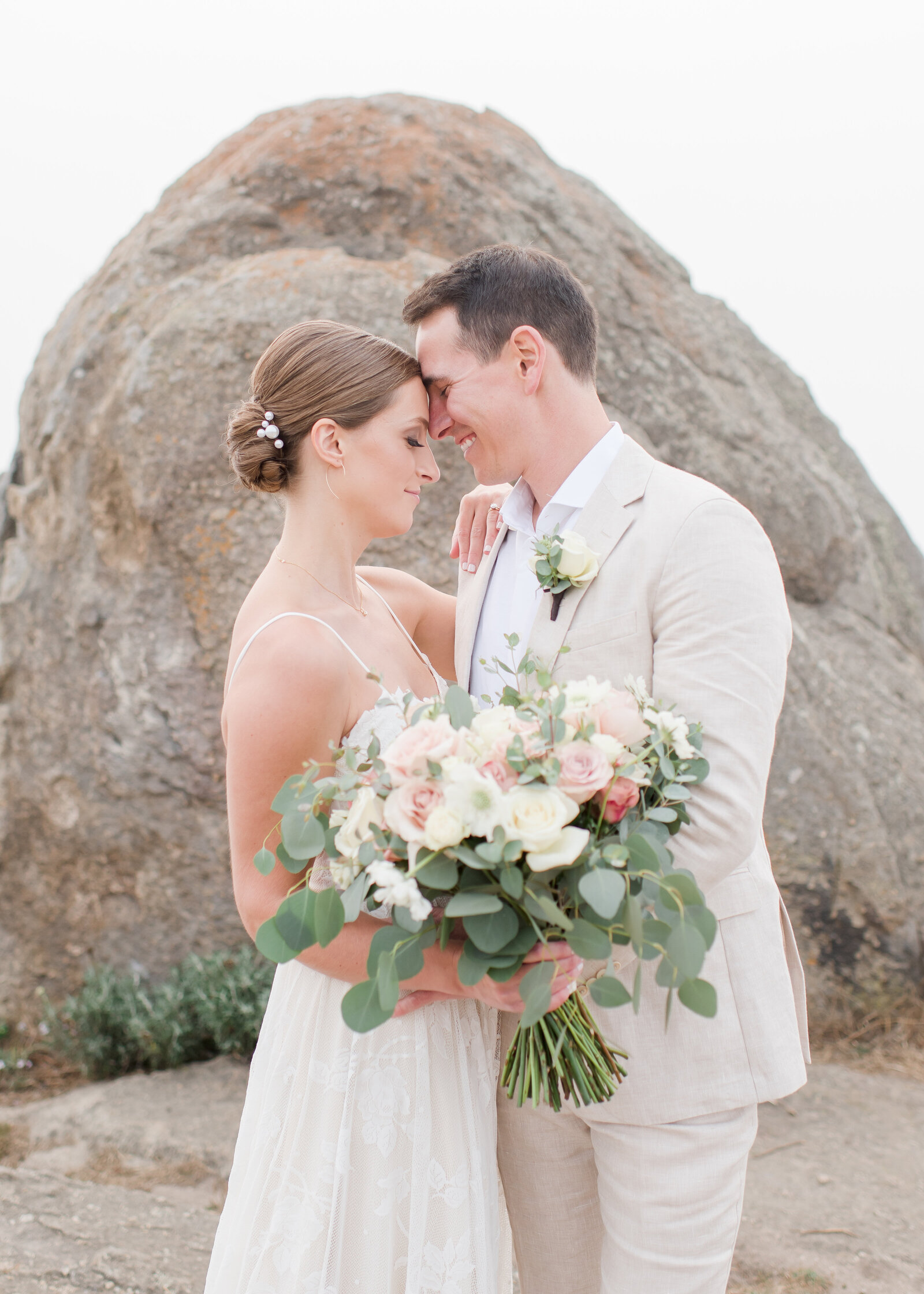 couple cuddling together in front of rock on their monterey beach wedding