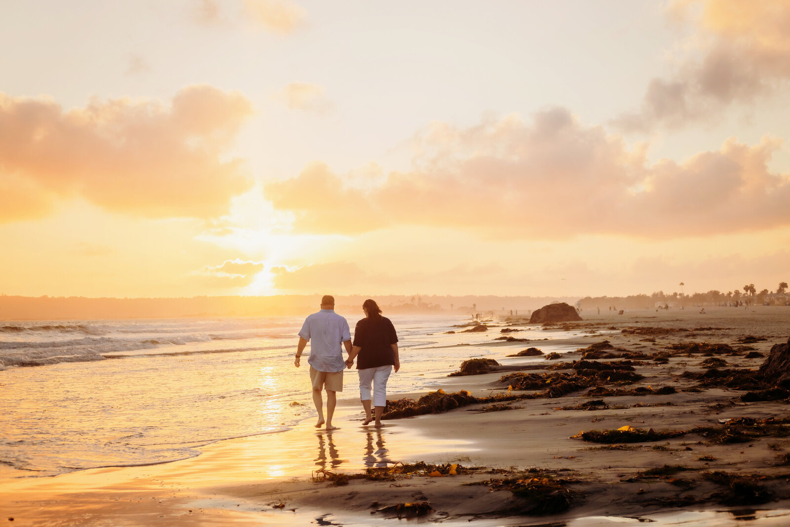 Family Photographer, a couple hold hands and walk in the beach sand at sunset