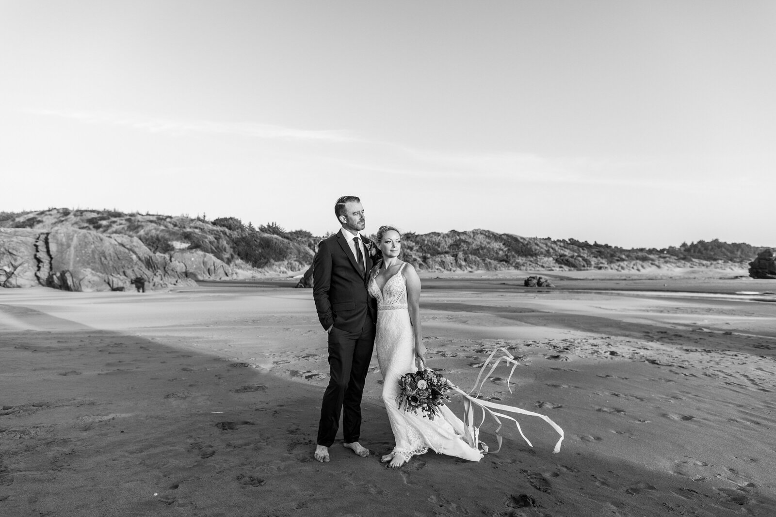 Newlyweds standing on windy beach